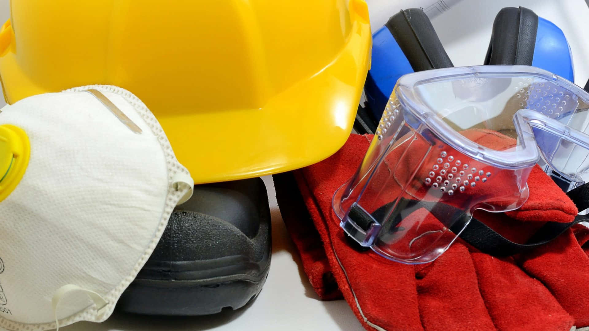 Safety 桌布 壁紙 — 白色表面上包括黃色安全帽、呼吸器、護目鏡和紅色手套的建築安全裝備特寫。