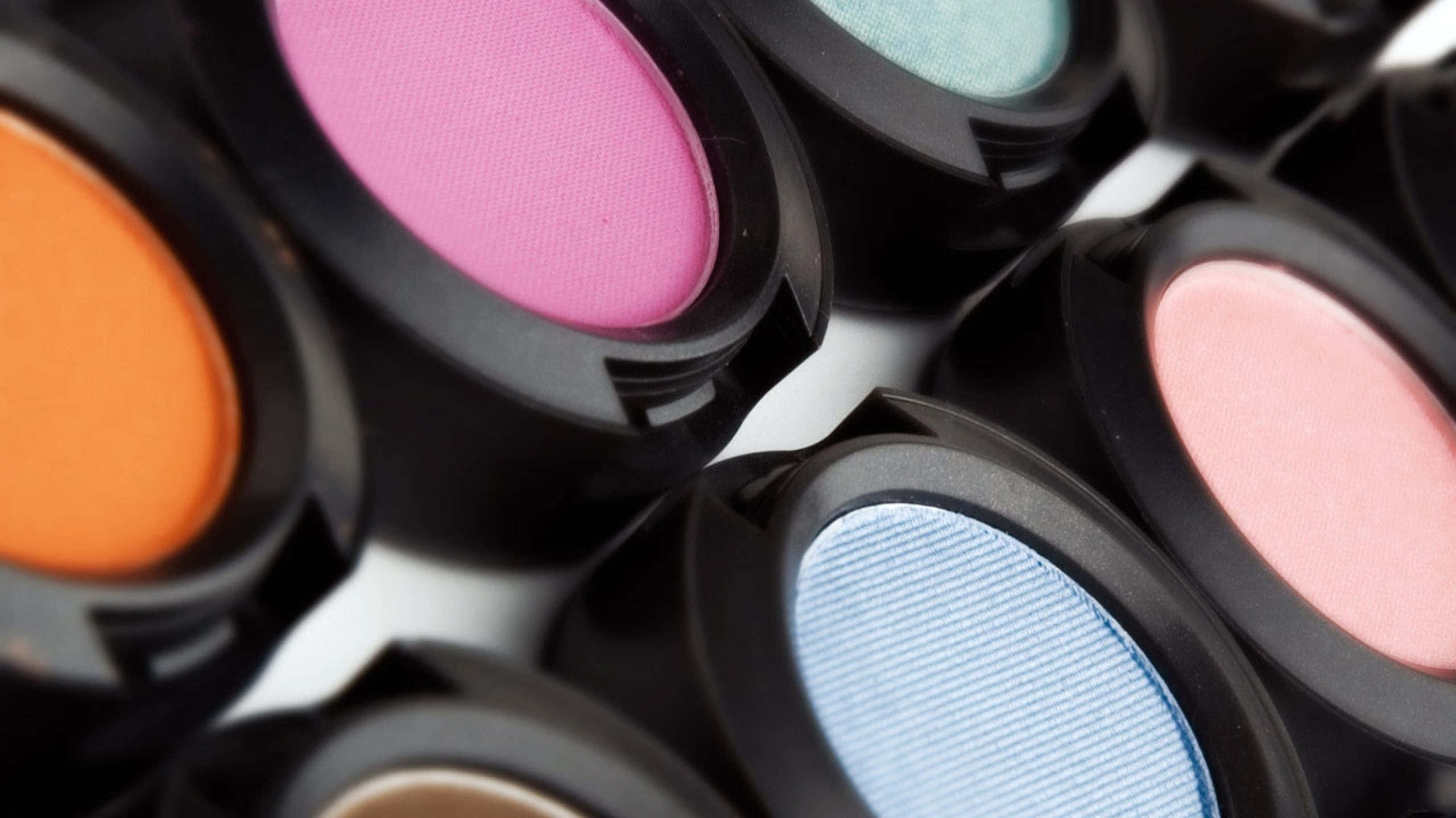 Mac Cosmetics 桌布 壁紙 — 白色表面上對角排列的黑色眼影盤中的彩色眼影特寫。