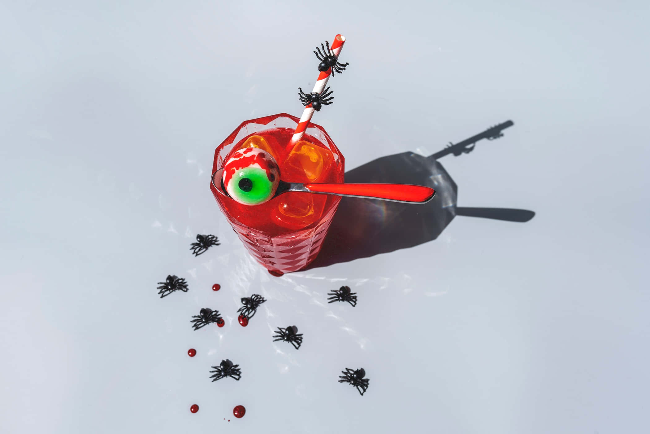 Halloween Drinks 桌布 壁紙 — 白色表面上的紅色萬聖節雞尾酒俯視圖，上面有糖果眼球和蜘蛛裝飾吸管。
