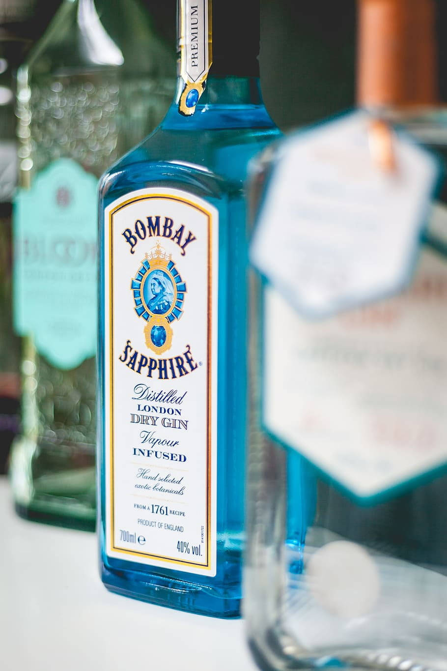bottle 桌布 壁紙 — 白色表面上藍色 Bombay Sapphire 琴酒瓶的特寫，背景瓶子模糊。