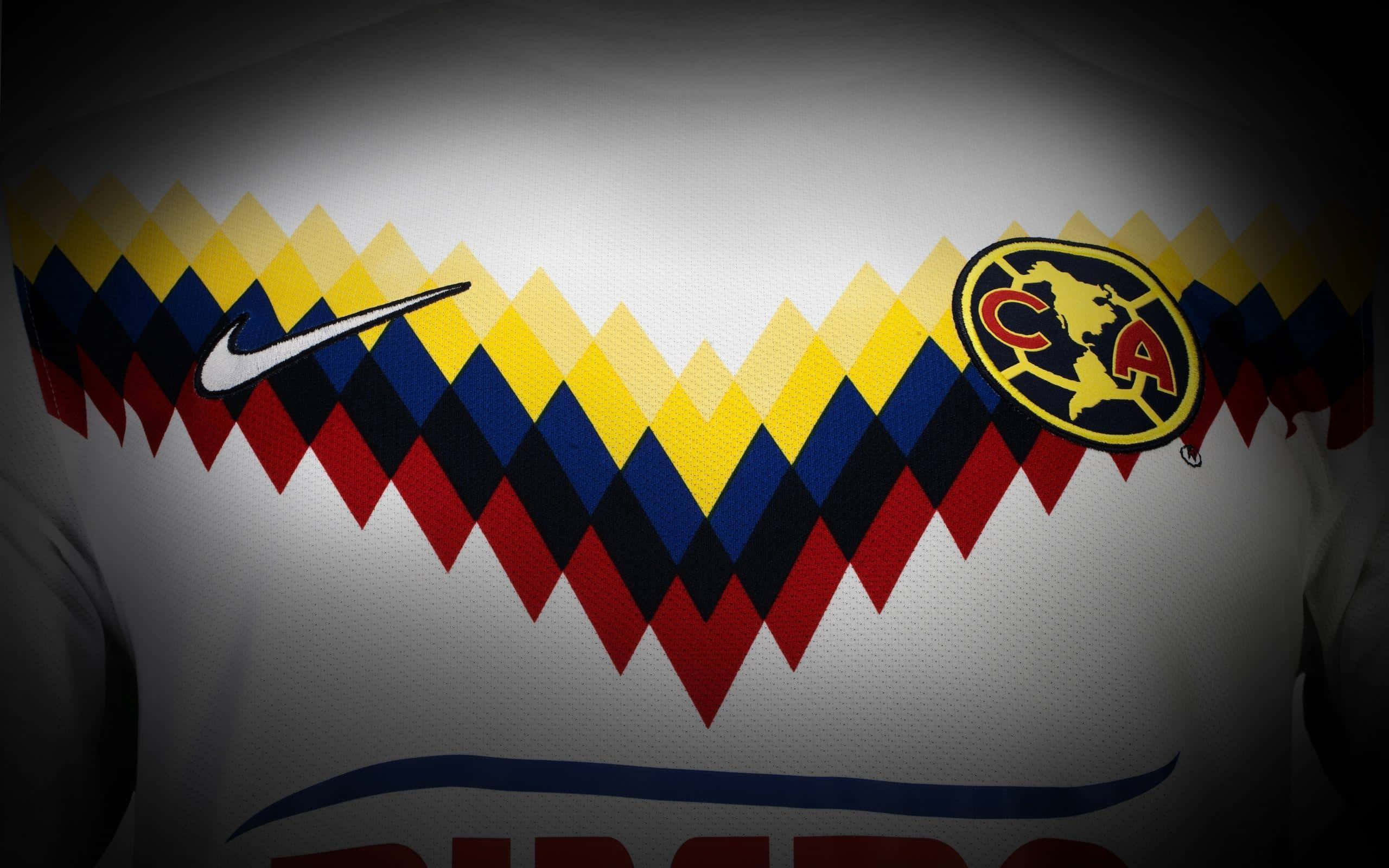 Club America 桌布 壁紙 — 白色足球球衣特寫，帶有醒目的紅、黃、藍色鋸齒圖案、Nike 勾勾和 Club America 徽章，在戲劇性的聚光燈下。
