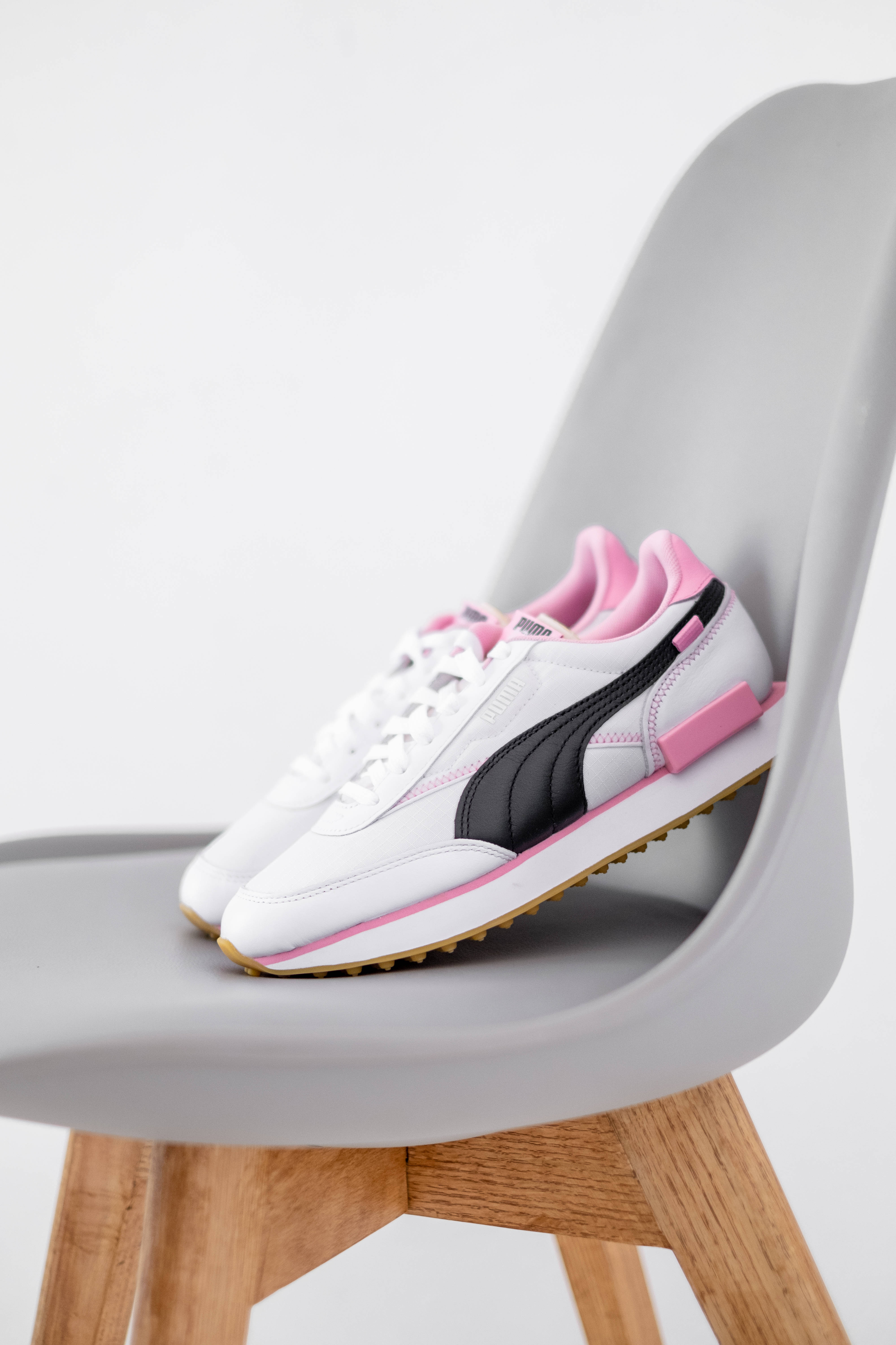 Puma 桌布 壁紙 — 白色運動鞋帶有粉紅色和黑色點綴，隨意地放在一張現代灰色木腿椅子上。