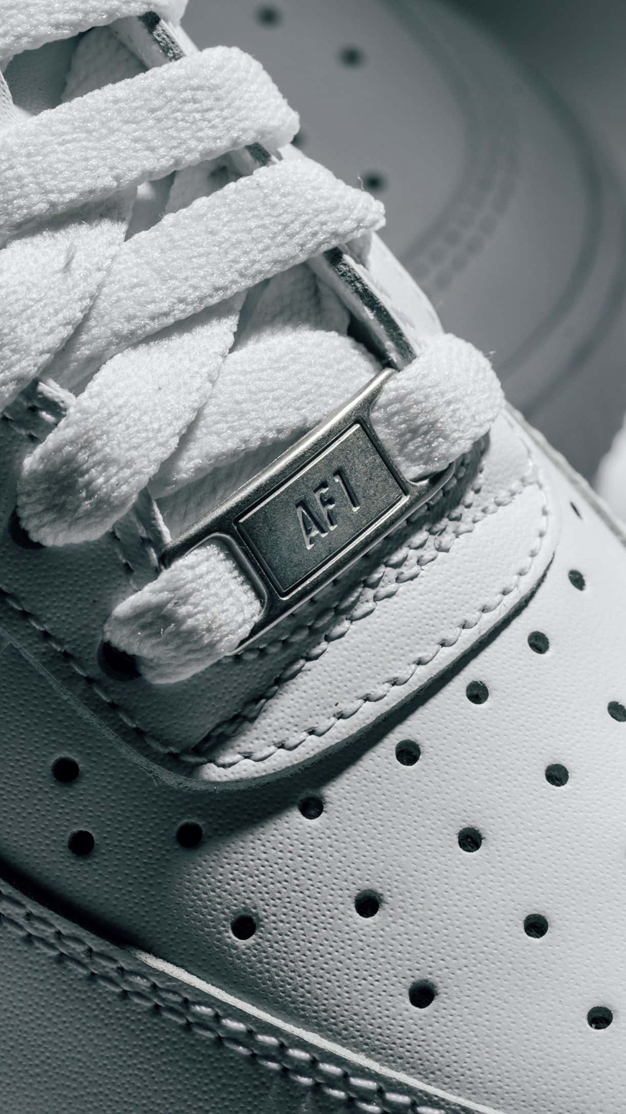 Nike Air Force 桌布 壁紙 — 白色運動鞋特寫，帶有紋理鞋帶和金屬AF1標籤，在柔和燈光下。