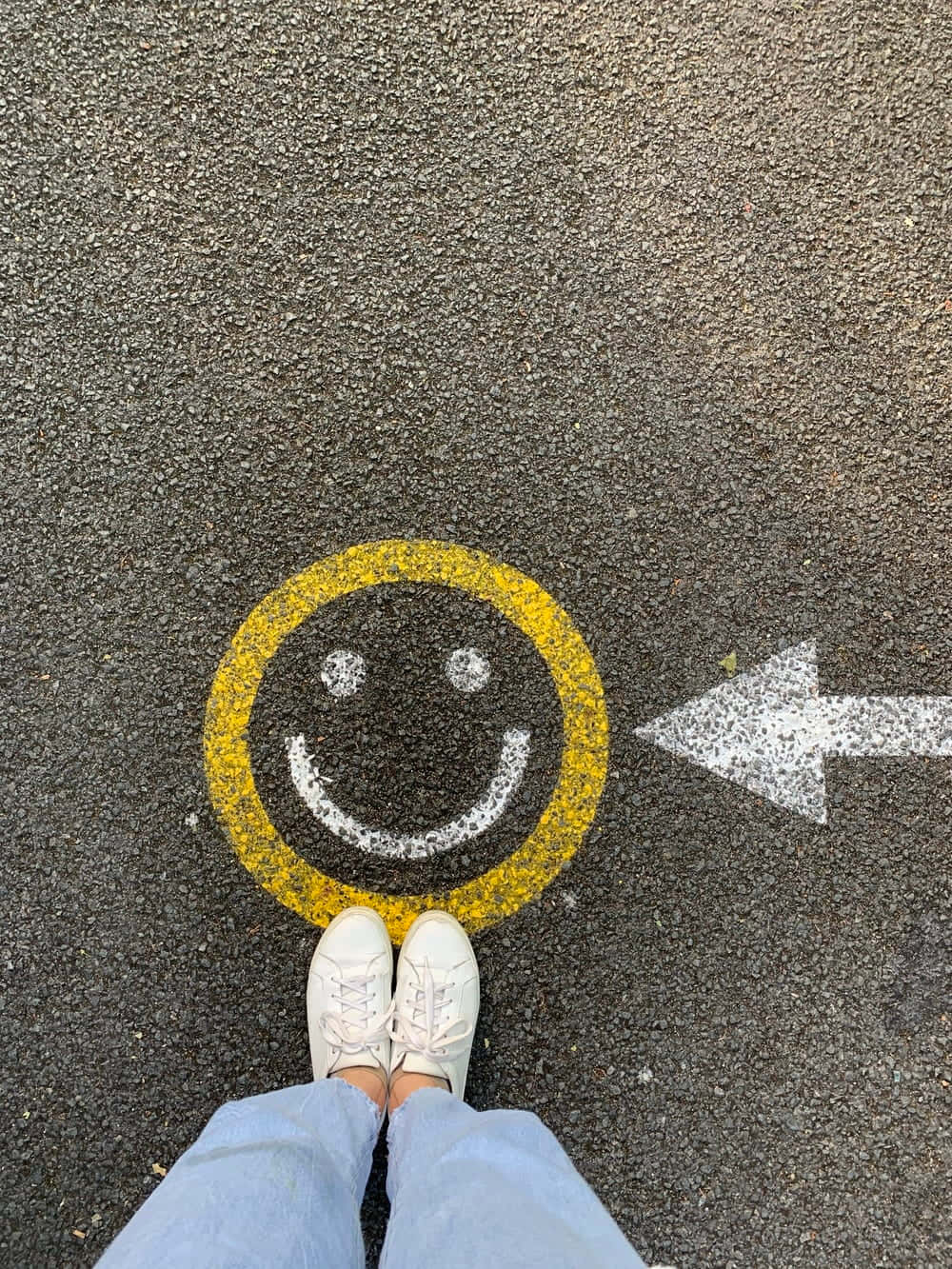 Aesthetic Smiley Face 桌布 壁紙 — 白色運動鞋站在瀝青上，旁邊有一個黃色笑臉和一個指向左邊的白色箭頭。