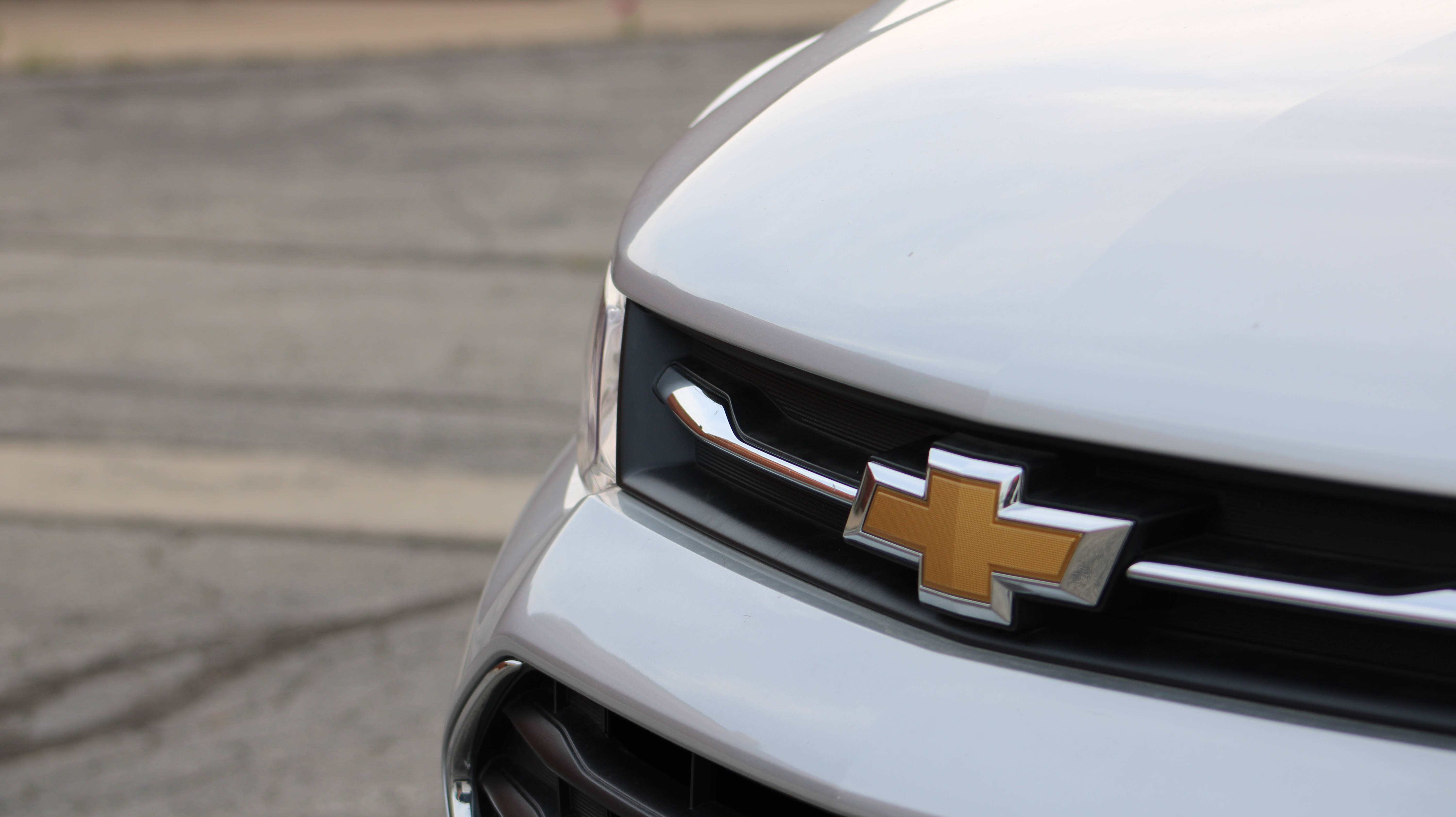 Chevrolet Logo 桌布 壁紙 — 白色雪佛蘭汽車前格柵的特寫，帶有金色蝴蝶結標誌，背景為模糊的瀝青路面。