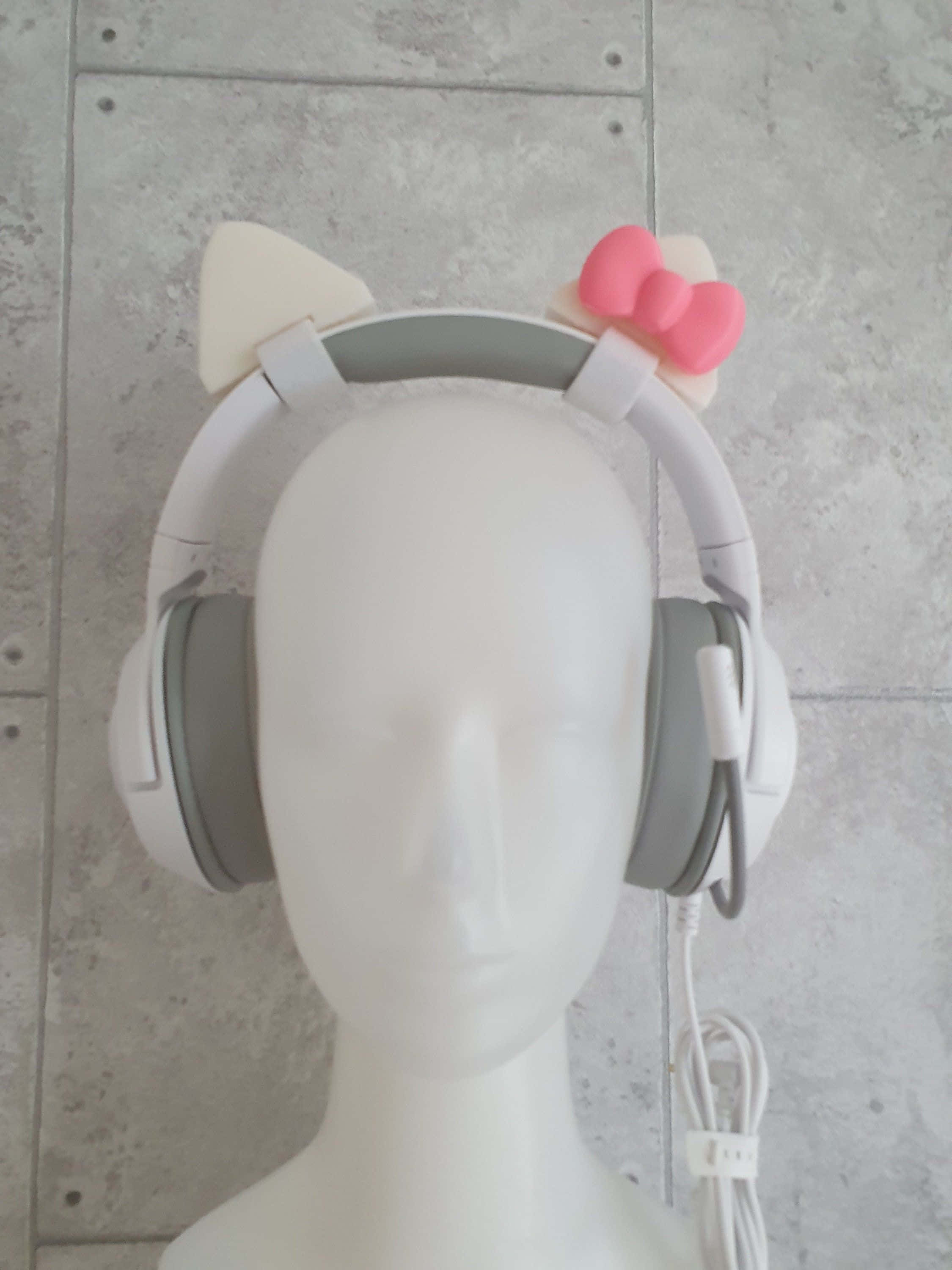 Gaming Accessories 桌布 壁紙 — 白色頭戴式耳機，帶有貓耳和粉紅色蝴蝶結，展示在灰色瓷磚牆前的模特兒頭上。