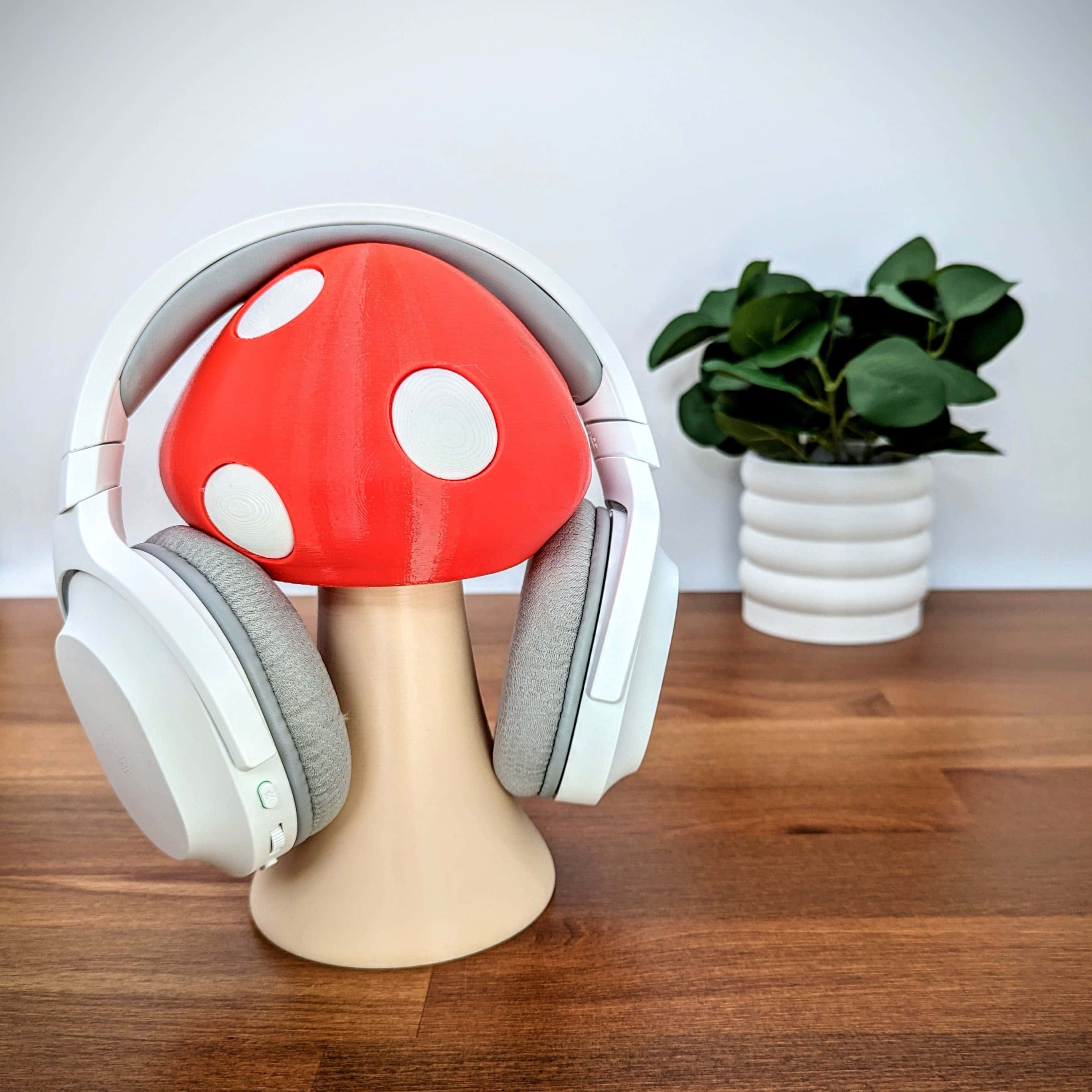 Gaming Accessories 桌布 壁紙 — 白色頭戴式耳機放在一個紅白蘑菇形支架上，旁邊是木桌上的一盆植物。