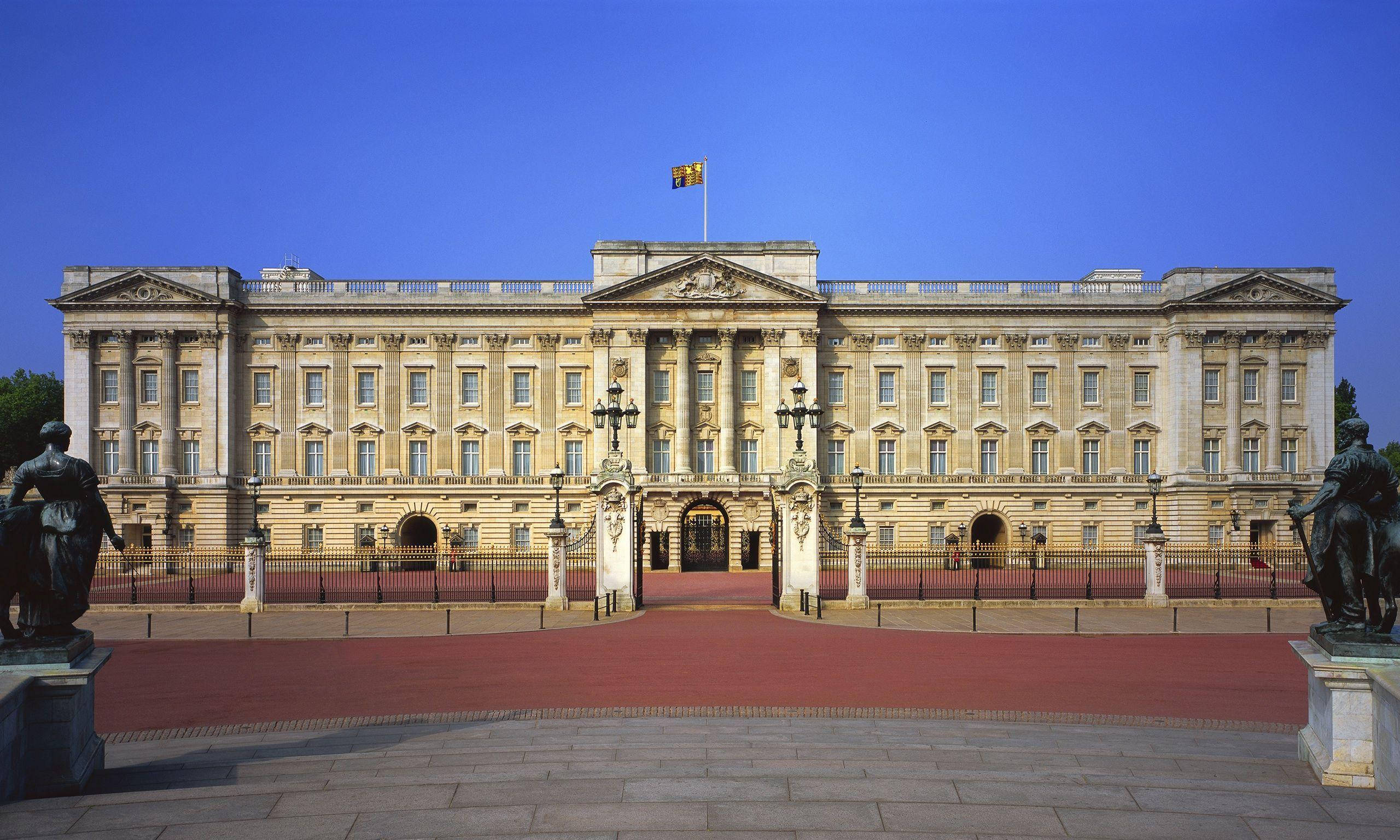 England 桌布 壁紙 — 白金漢宮宏偉的外牆，在晴朗的藍天下，入口兩側鋪有紅地毯和雕像。