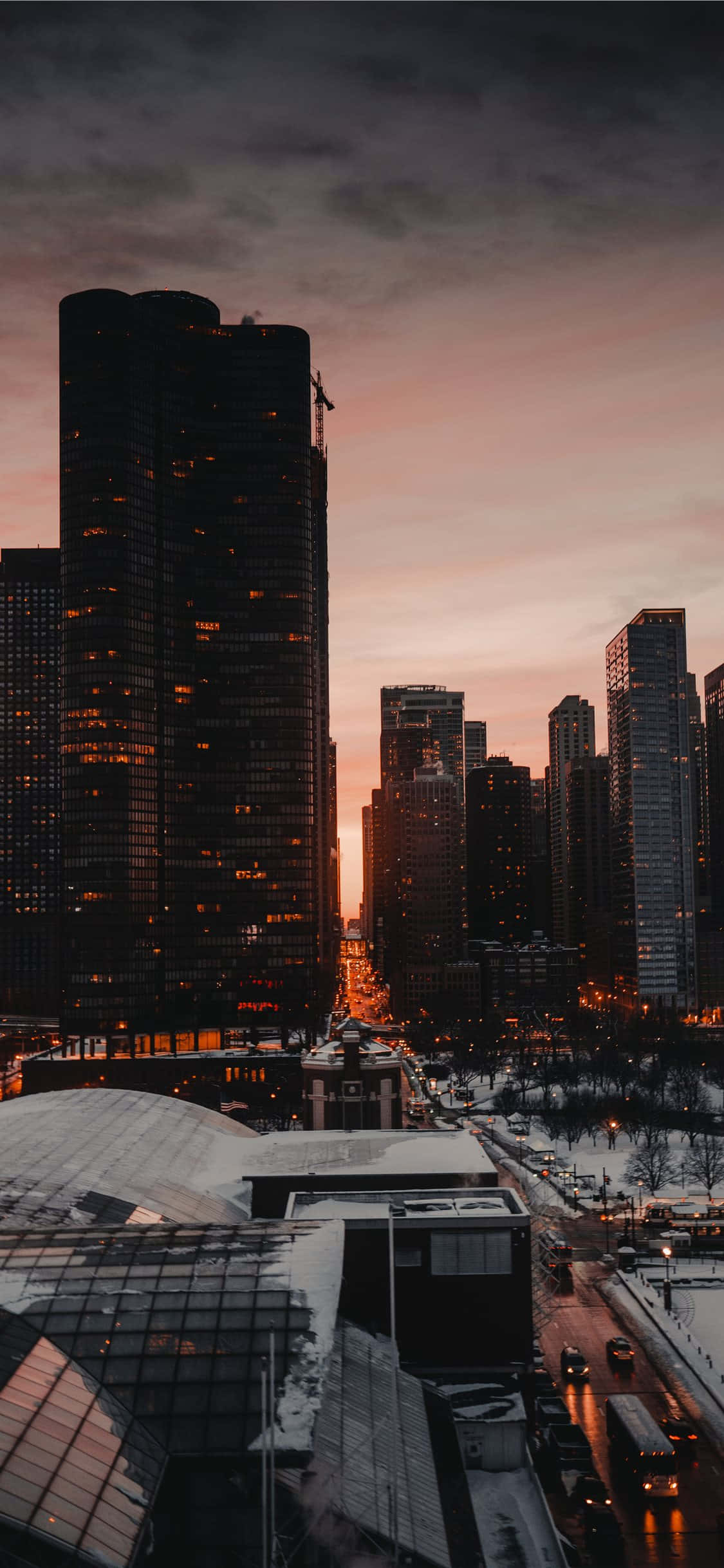 USA iPhone 桌布 壁紙 — 白雪覆蓋城市街道，摩天大樓在暮色中映襯著粉紅與橙色的天空。