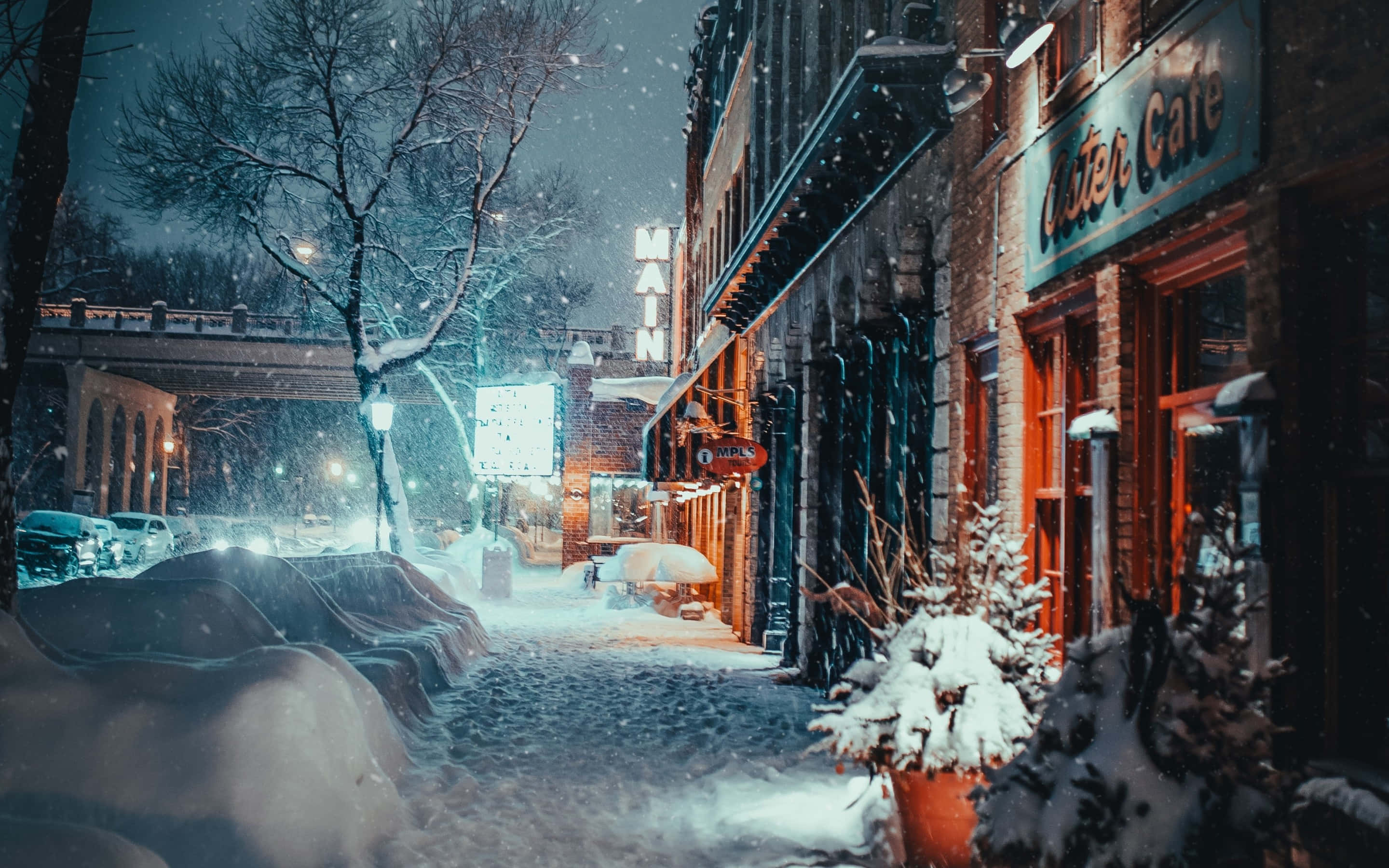 blizzard 桌布 壁紙 — 白雪覆蓋寧靜的城市街道，夜晚時分，店舖櫥窗的溫暖燈光映照著飄落的雪花。