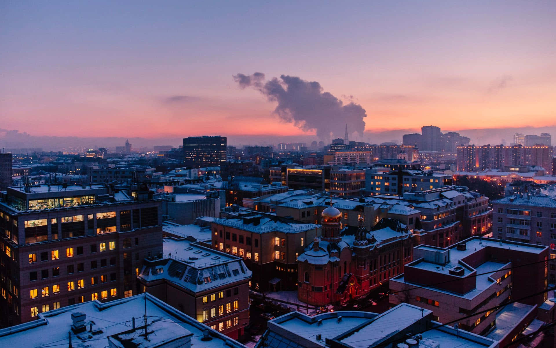 Rooftop 桌布 壁紙 — 白雪覆蓋屋頂，城市燈光在帶有粉紅和紫色色調的暮色天空中閃耀。