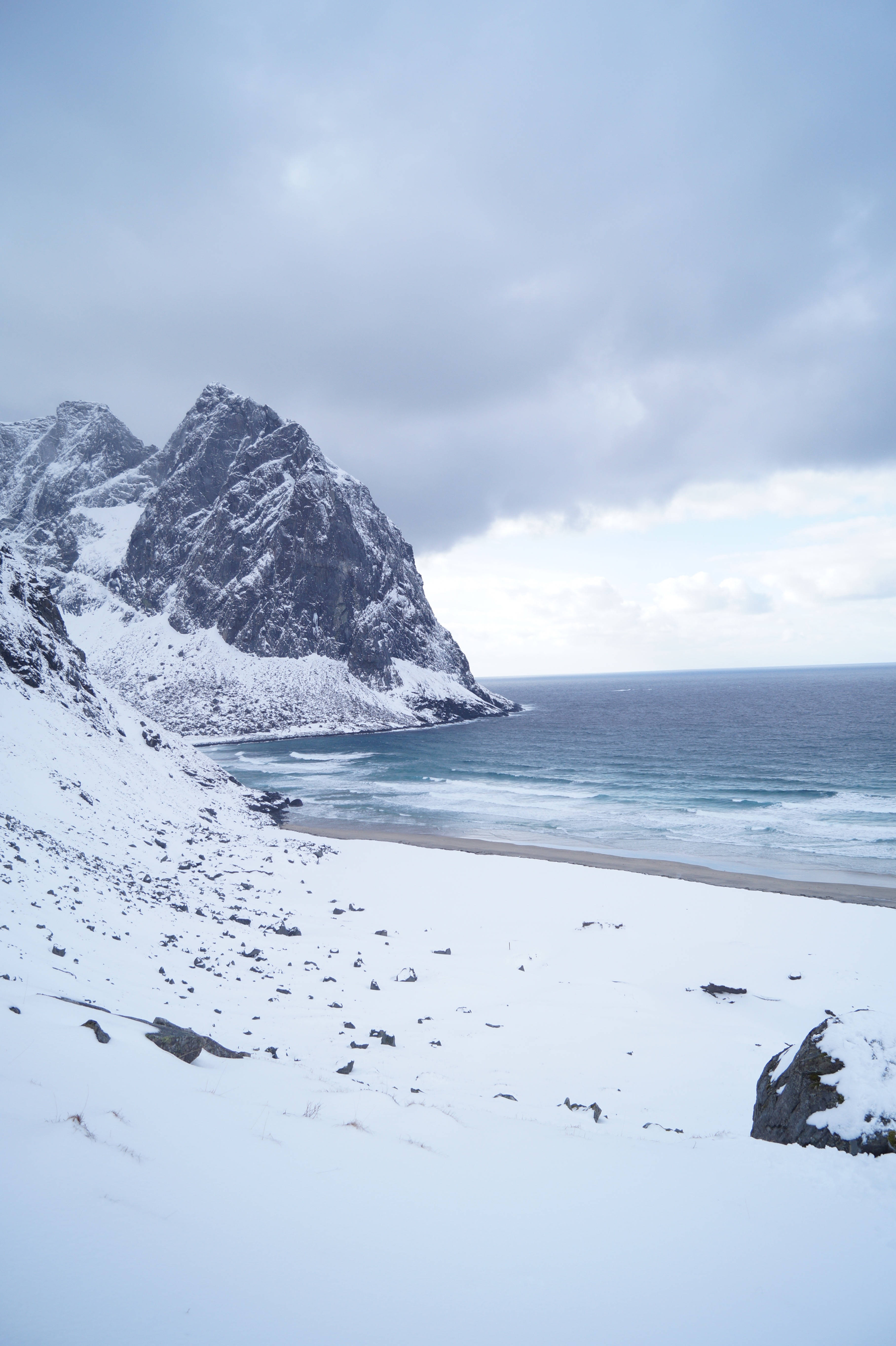 Norway 桌布 壁紙 — 白雪覆蓋崎嶇的懸崖和沙灘，海浪在陰沉的冬日天空下拍打著海岸。