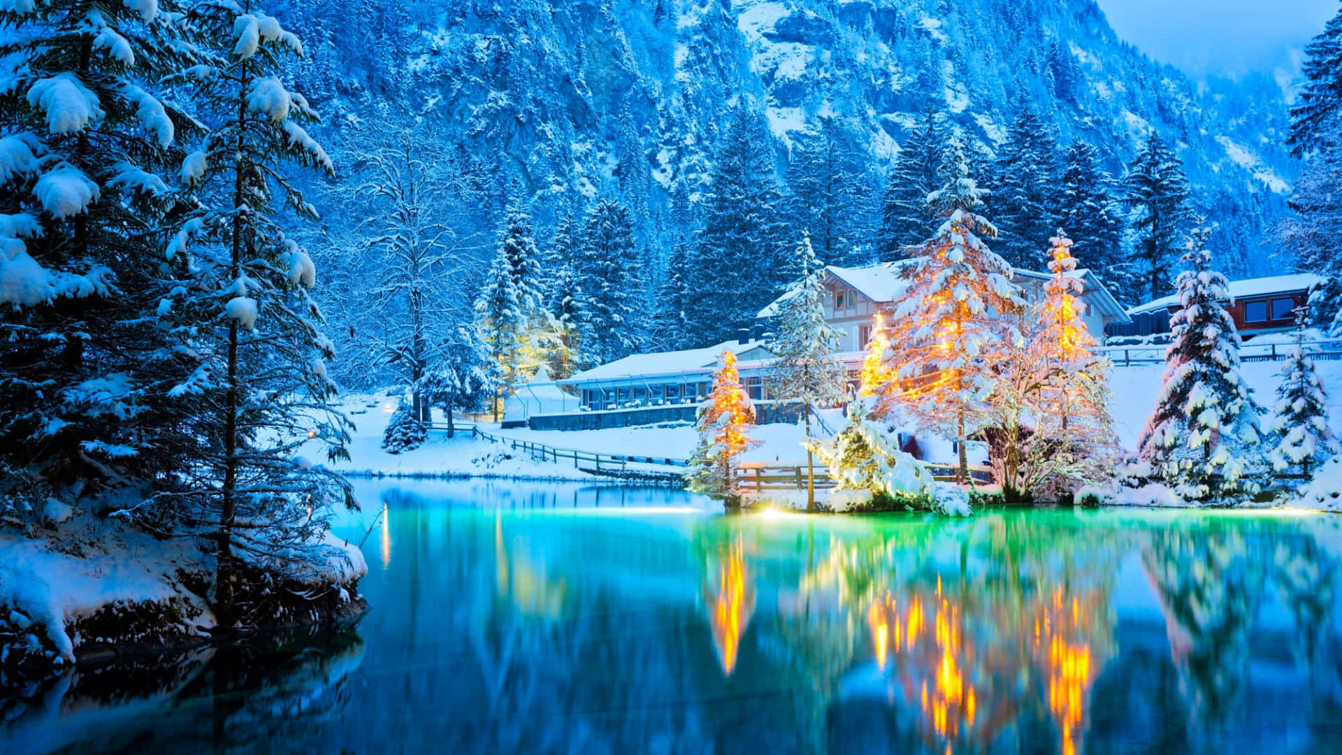 Winter Aesthetic 桌布 壁紙 — 白雪覆蓋松樹和木屋，旁邊的玻璃般湖面在黃昏時反射溫暖的金色燈光。