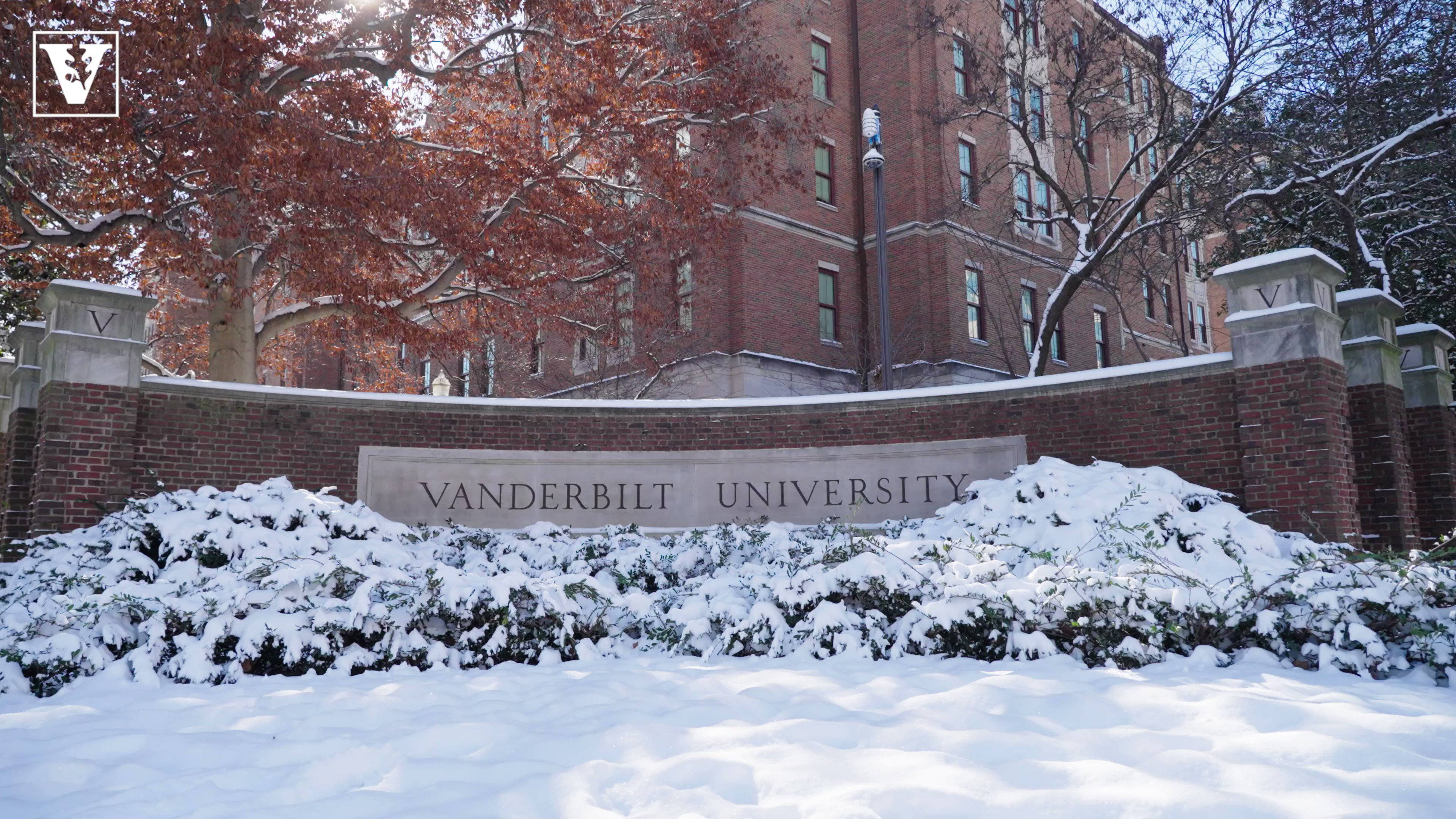 冬天 桌布 壁紙 — 白雪覆蓋灌木叢和一面帶有 'VANDERBILT UNIVERSITY' 標誌的磚牆，前面是一座紅磚校園建築，周圍有秋樹。