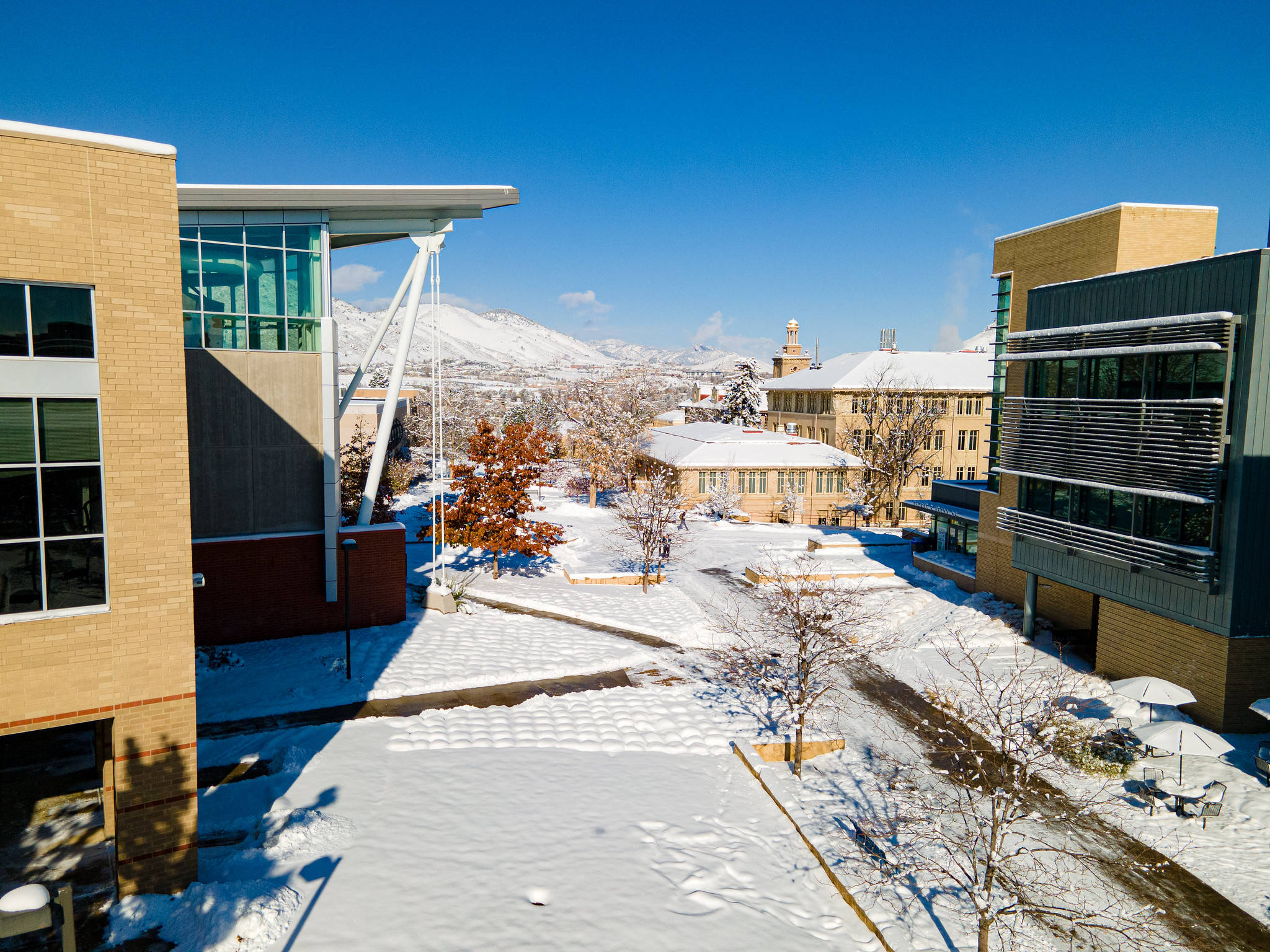 Building 桌布 壁紙 — 白雪覆蓋現代校園庭院，藍天清澈，遠方有積雪的山峰。