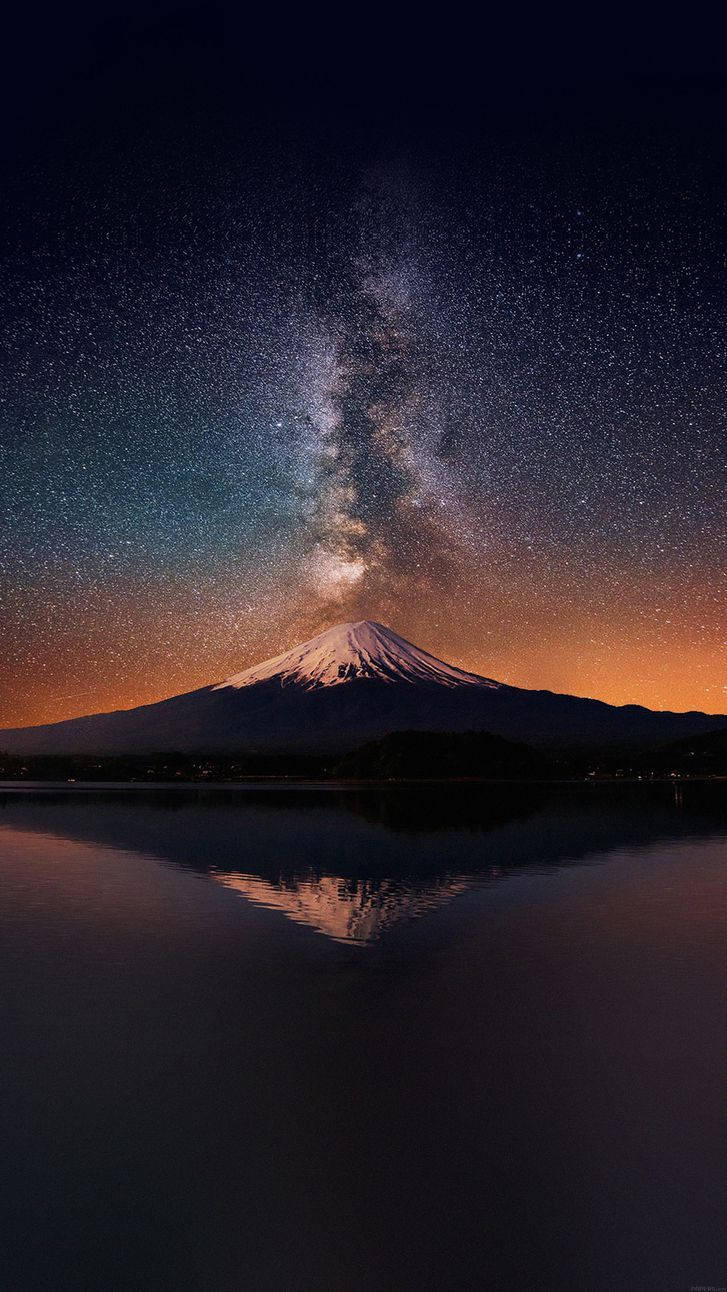 top iPhone 桌布 壁紙 — 白雪覆蓋的富士山在平靜的水面上完美倒映，上方是燦爛星空，銀河拱橋般橫跨天際。