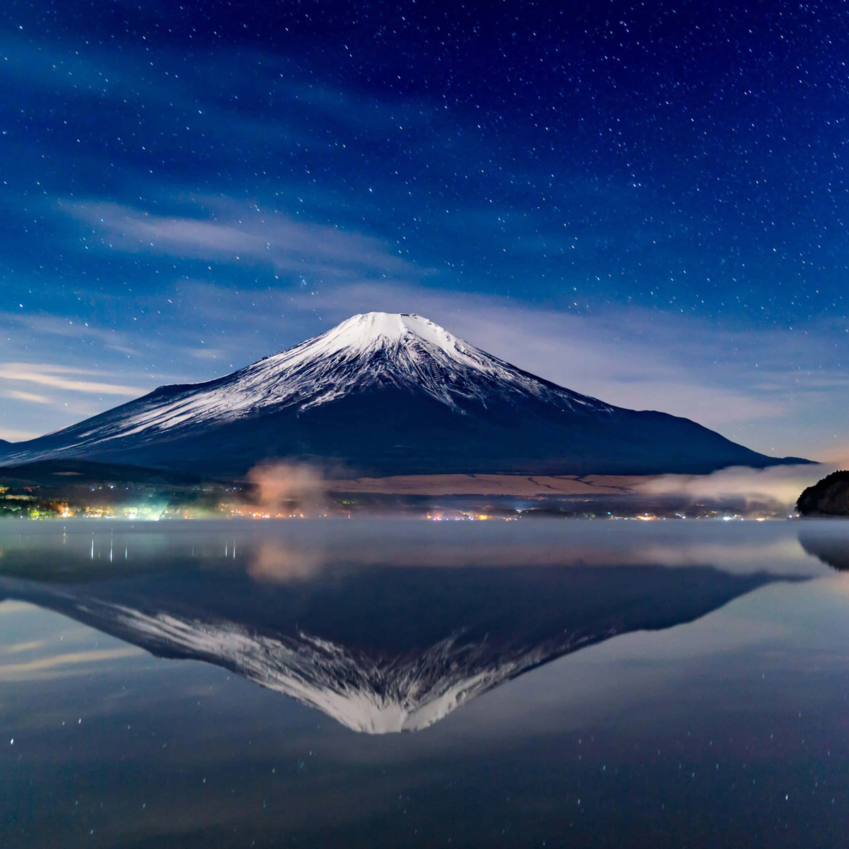 Mt Fuji 桌布 壁紙 — 白雪覆蓋的富士山在平靜的湖面上完美倒映，下方是繁星點點的夜空和微弱的城市燈光。