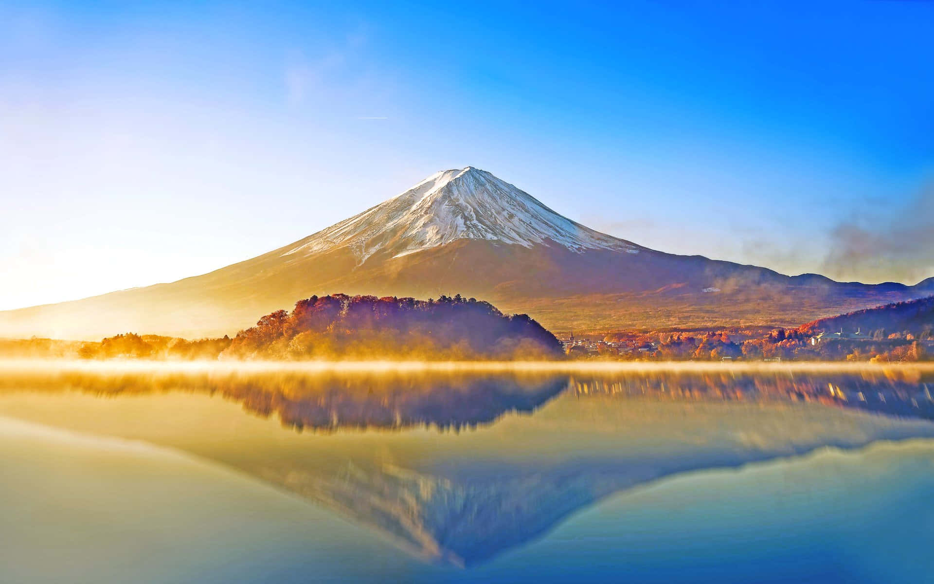 富士山 桌布 壁紙 — 白雪覆蓋的富士山在日出時分雄偉地聳立於霧氣繚繞的湖面上，呈現完美倒影和金色光芒。