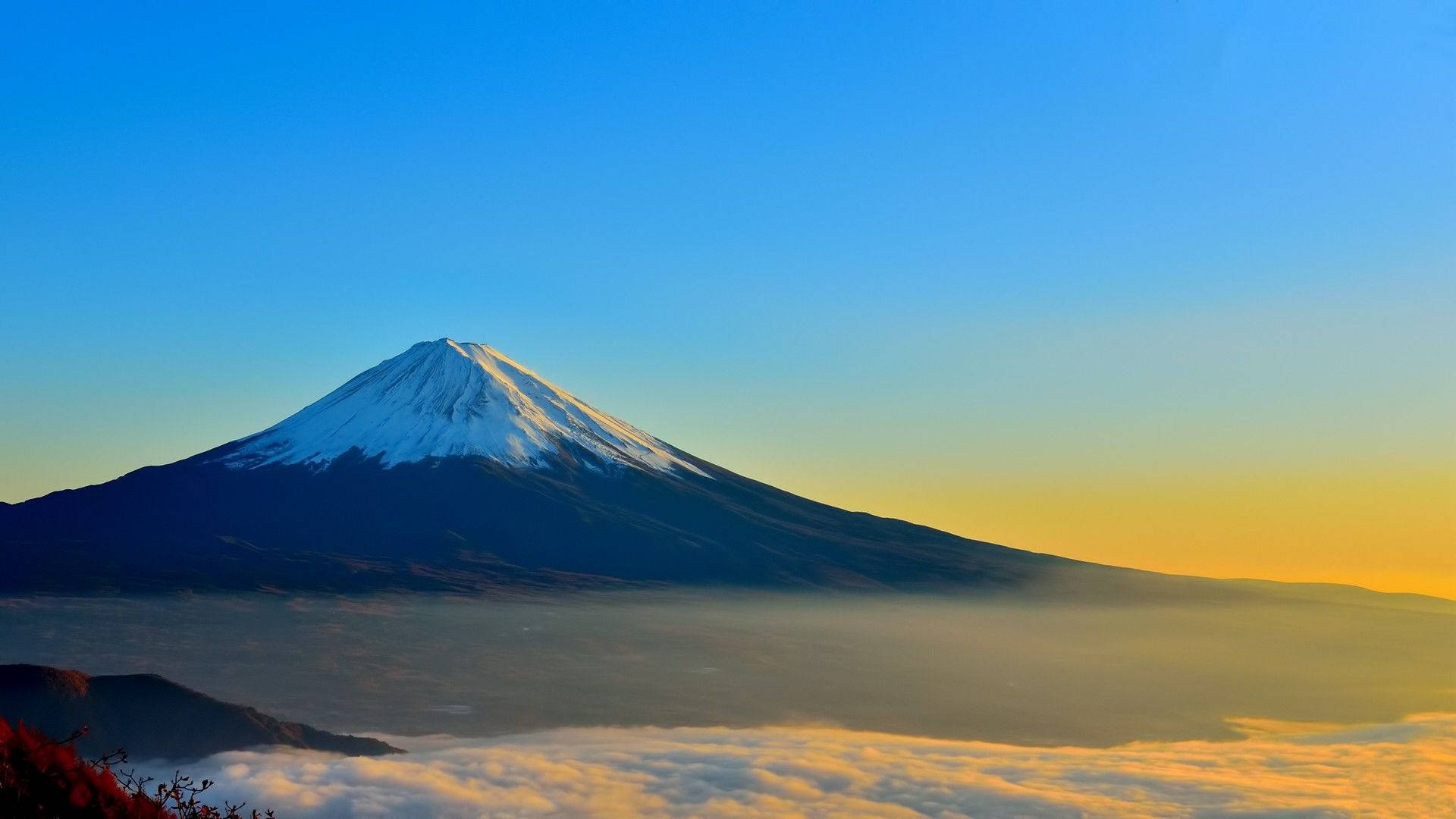 日本 桌布 壁紙 — 白雪覆蓋的富士山在晴朗的藍天下，於日出時分雄偉地聳立在金色雲海之上。