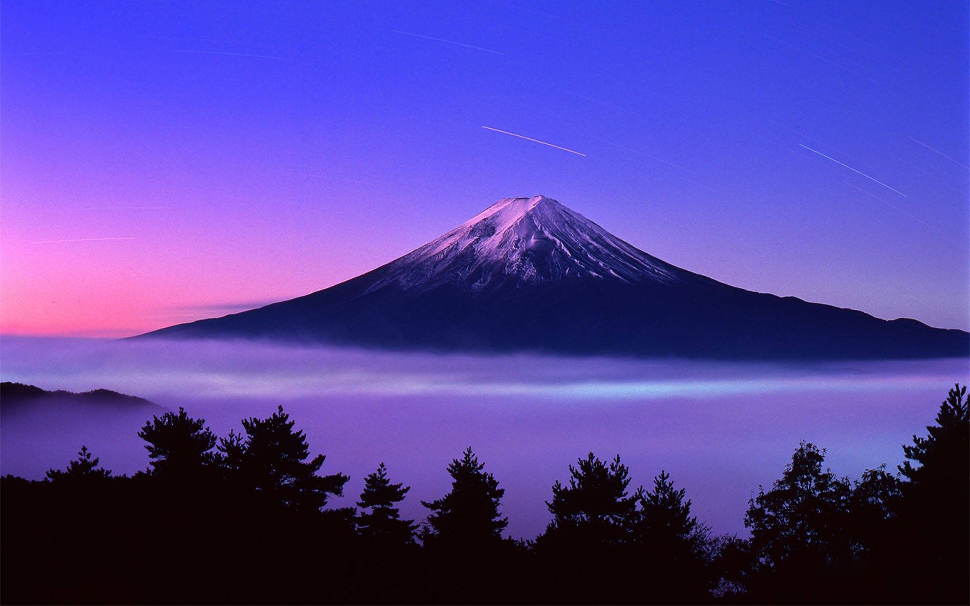 富士山 桌布 壁紙 — 白雪覆蓋的富士山在暮色中雄偉地聳立在霧海之上，天空呈現鮮豔的紫色和粉紅色。