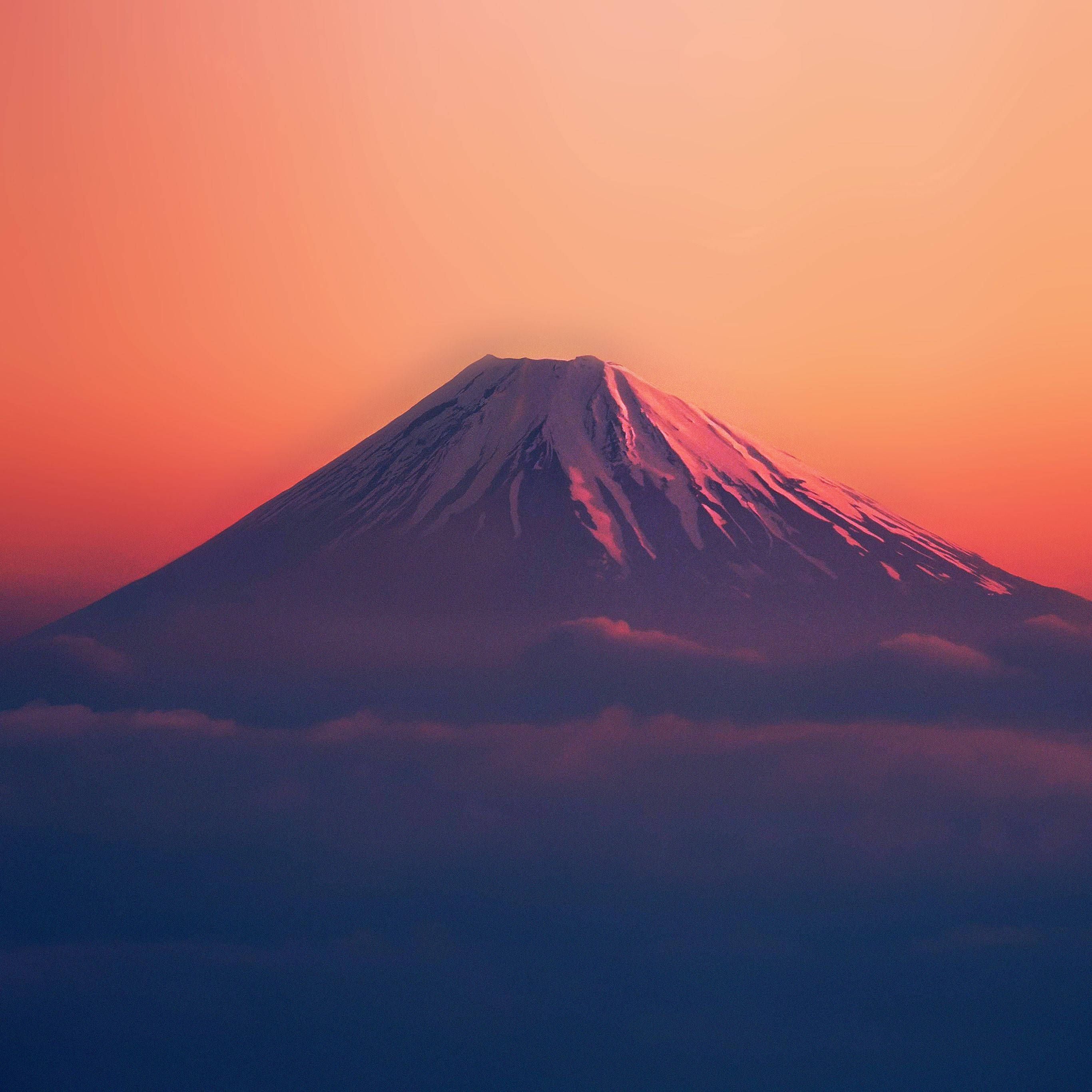紅色山脈 桌布 壁紙 — 白雪覆蓋的富士山在沐浴在溫暖橙色和粉紅色日落色調的雲海中雄偉地聳立。