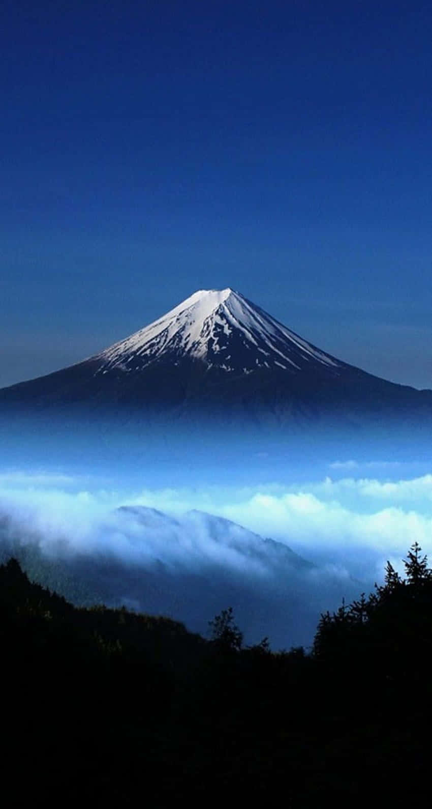 日本 桌布 壁紙 — 白雪覆蓋的富士山在深藍色暮色天空下，莊嚴地聳立在雲海之上。