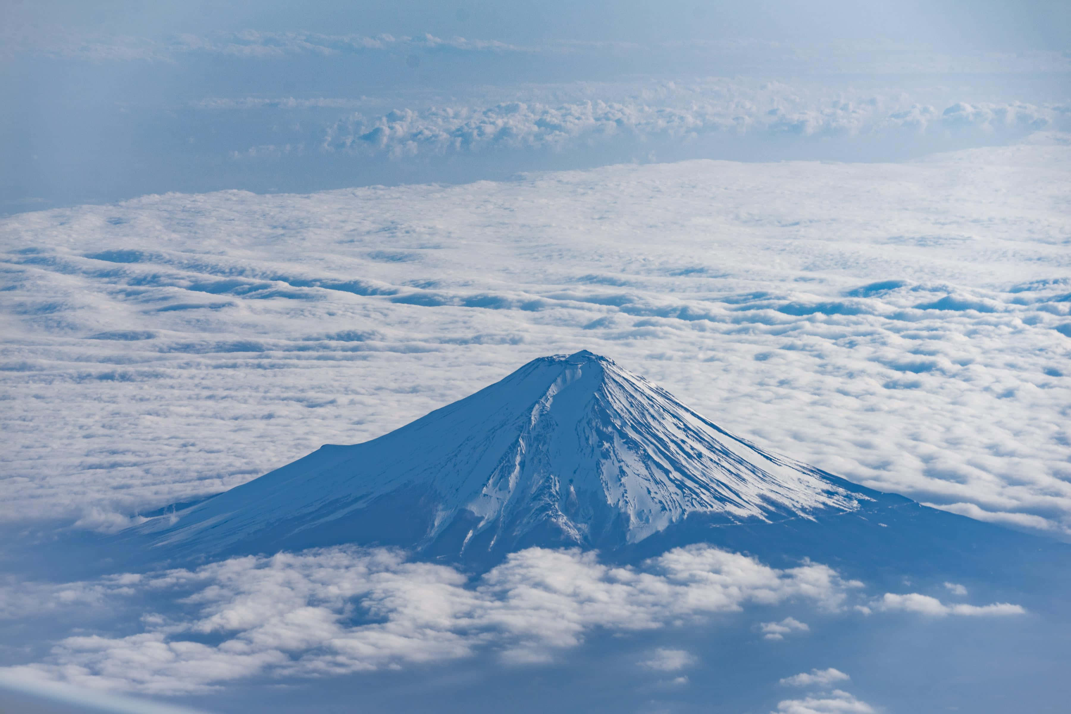 Mt Fuji 桌布 壁紙 — 白雪覆蓋的富士山在清澈的藍天下，雄偉地聳立在蓬鬆的白雲海洋之上。