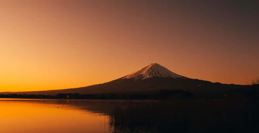 富士山 桌布 壁紙 — 白雪覆蓋的富士山在火紅橙色的日落映襯下形成剪影，其倒影在下方平靜的湖面上閃爍。