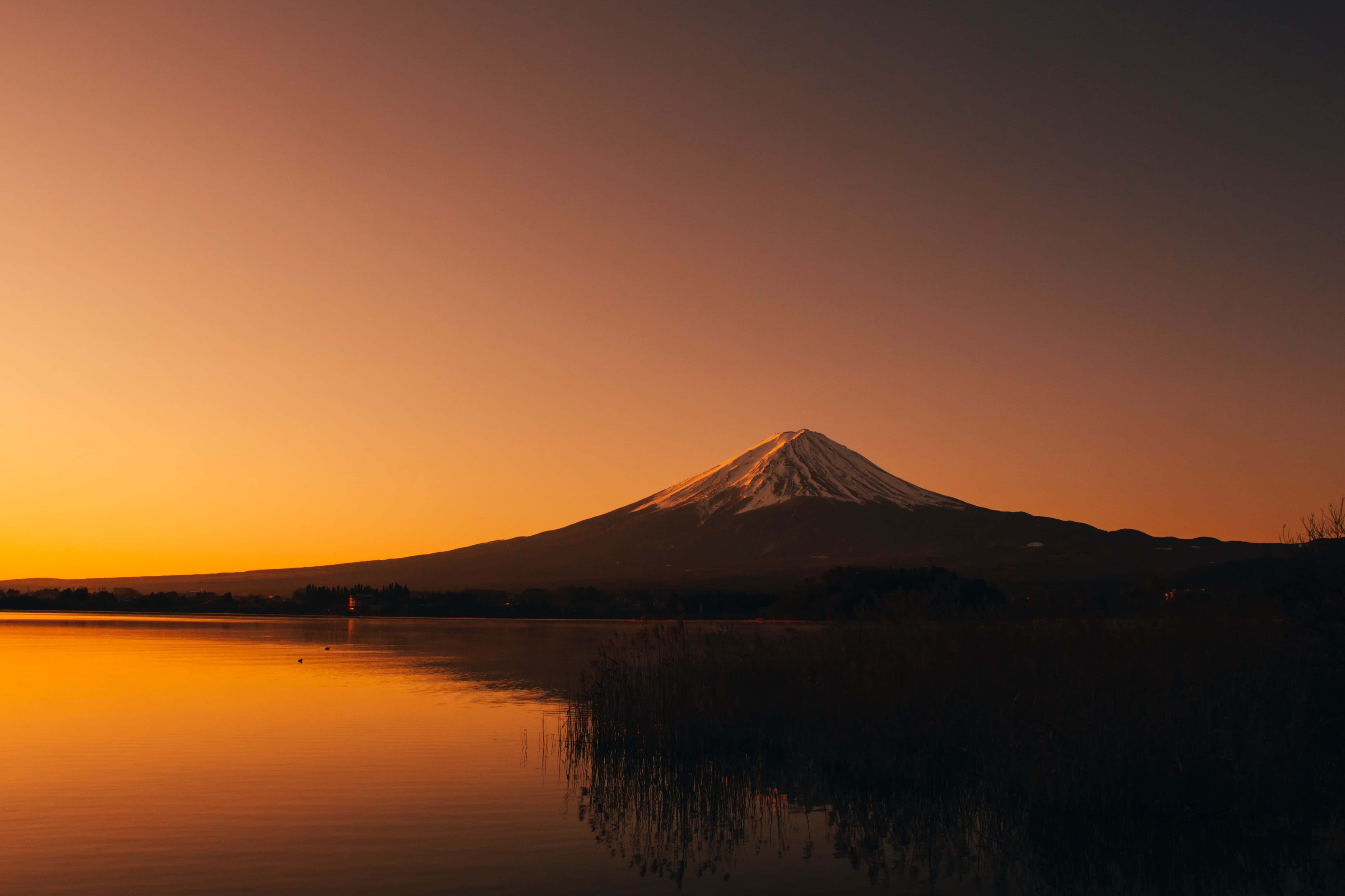 富士山 桌布 壁紙 — 白雪覆蓋的富士山在火紅的橙色日落映襯下形成剪影，其倒影在寧靜的湖面上閃爍。