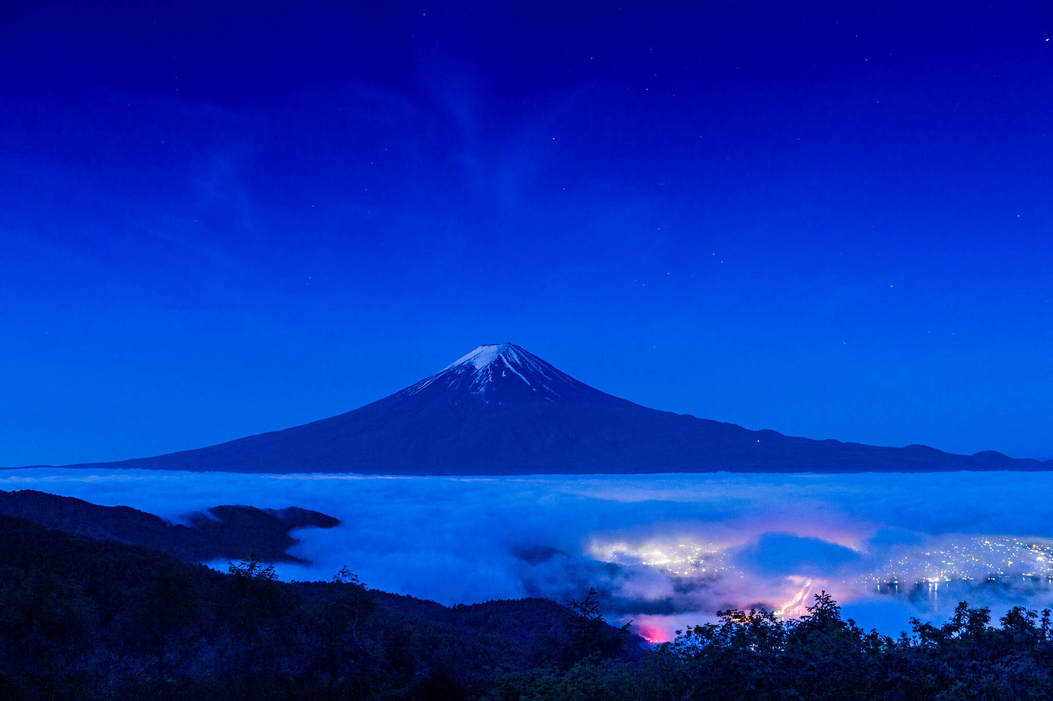 富士山 桌布 壁紙 — 白雪覆蓋的富士山在繁星點點的暮色天空下，雄偉地聳立在雲海之上，下方是閃爍的城市燈光。
