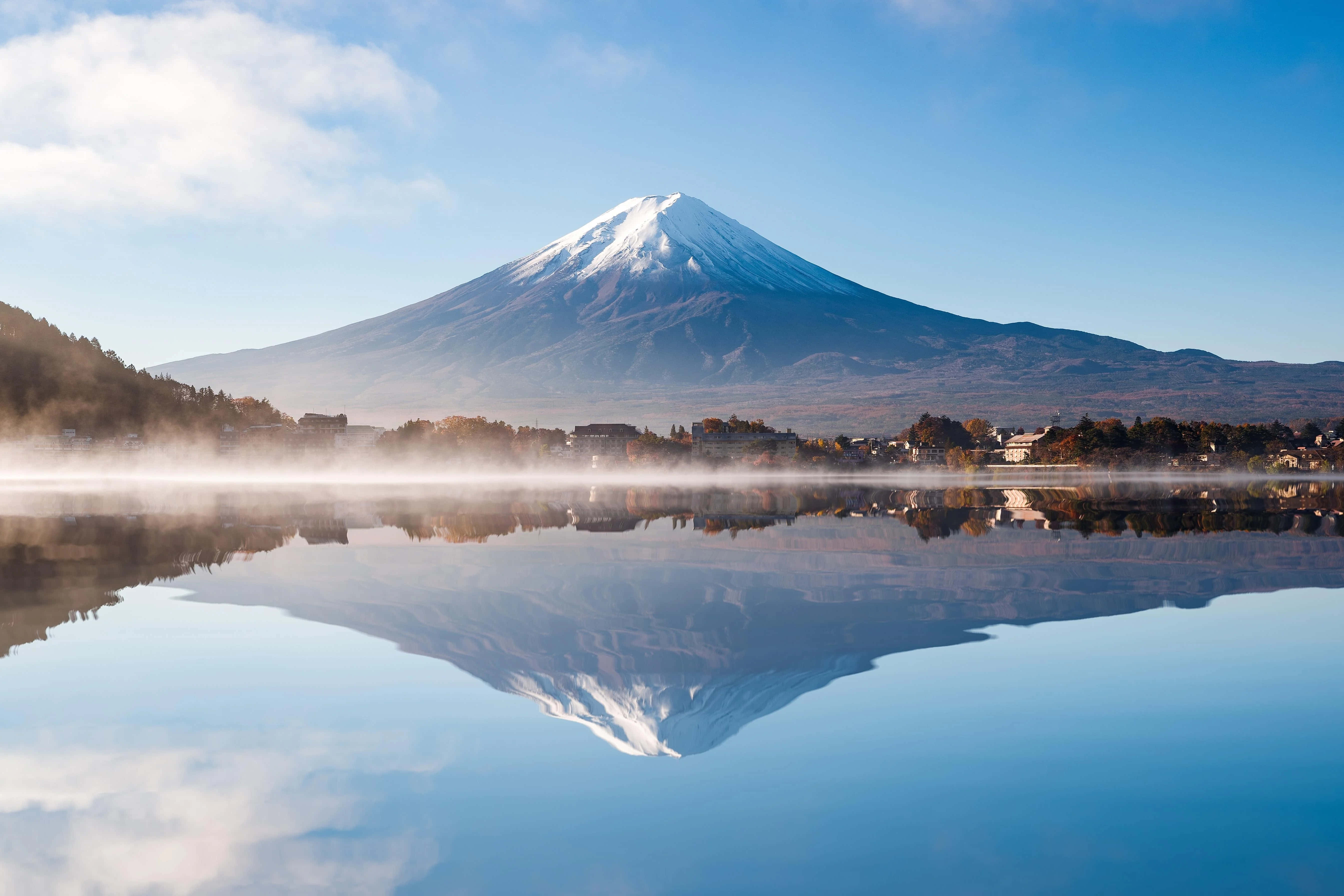 Mt Fuji 桌布 壁紙 — 白雪覆蓋的富士山在霧氣瀰漫的湖泊後方雄偉地升起，在清澈的藍天下映照出其完美的錐形。