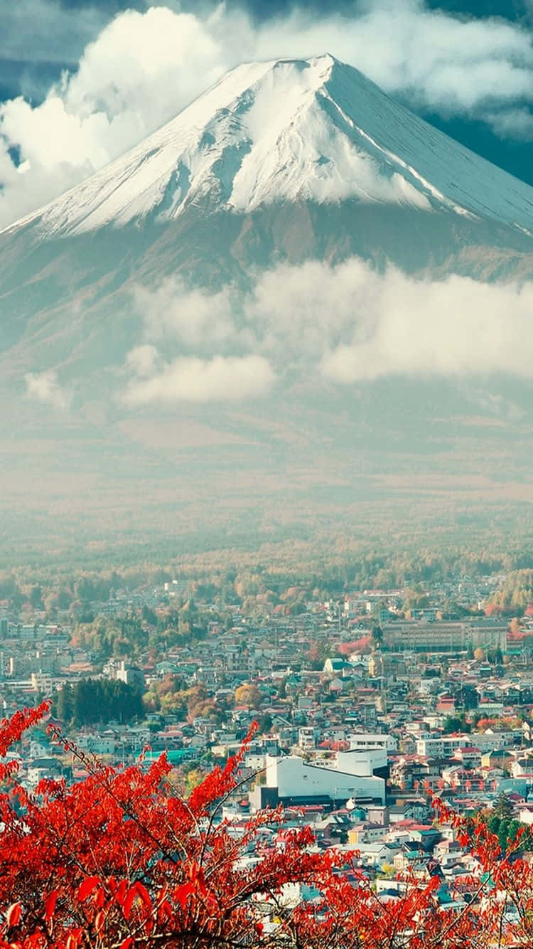 富士山 桌布 壁紙 — 白雪覆蓋的富士山雄偉地聳立在霧氣瀰漫的小鎮之上，前景是鮮豔的紅色秋葉。