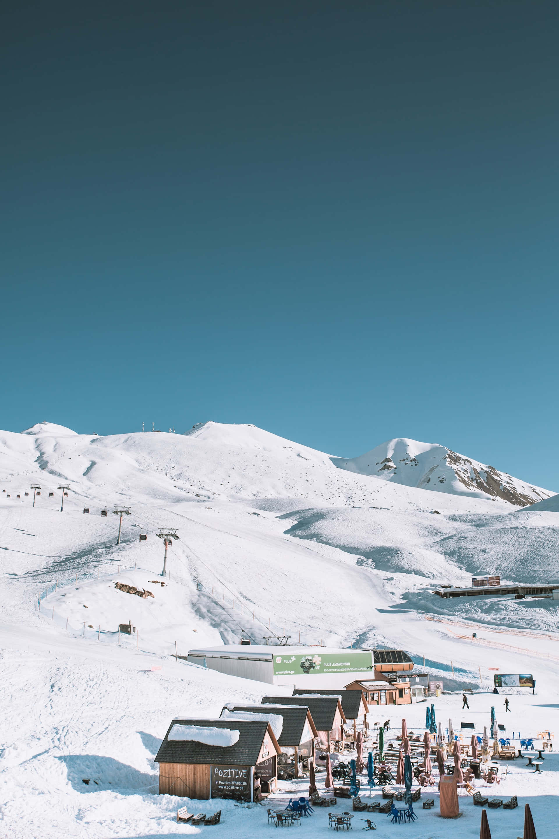 Ski Resort 桌布 壁紙 — 白雪覆蓋的山地滑雪度假村，設有木屋和滑雪纜車，在清澈的藍天下。