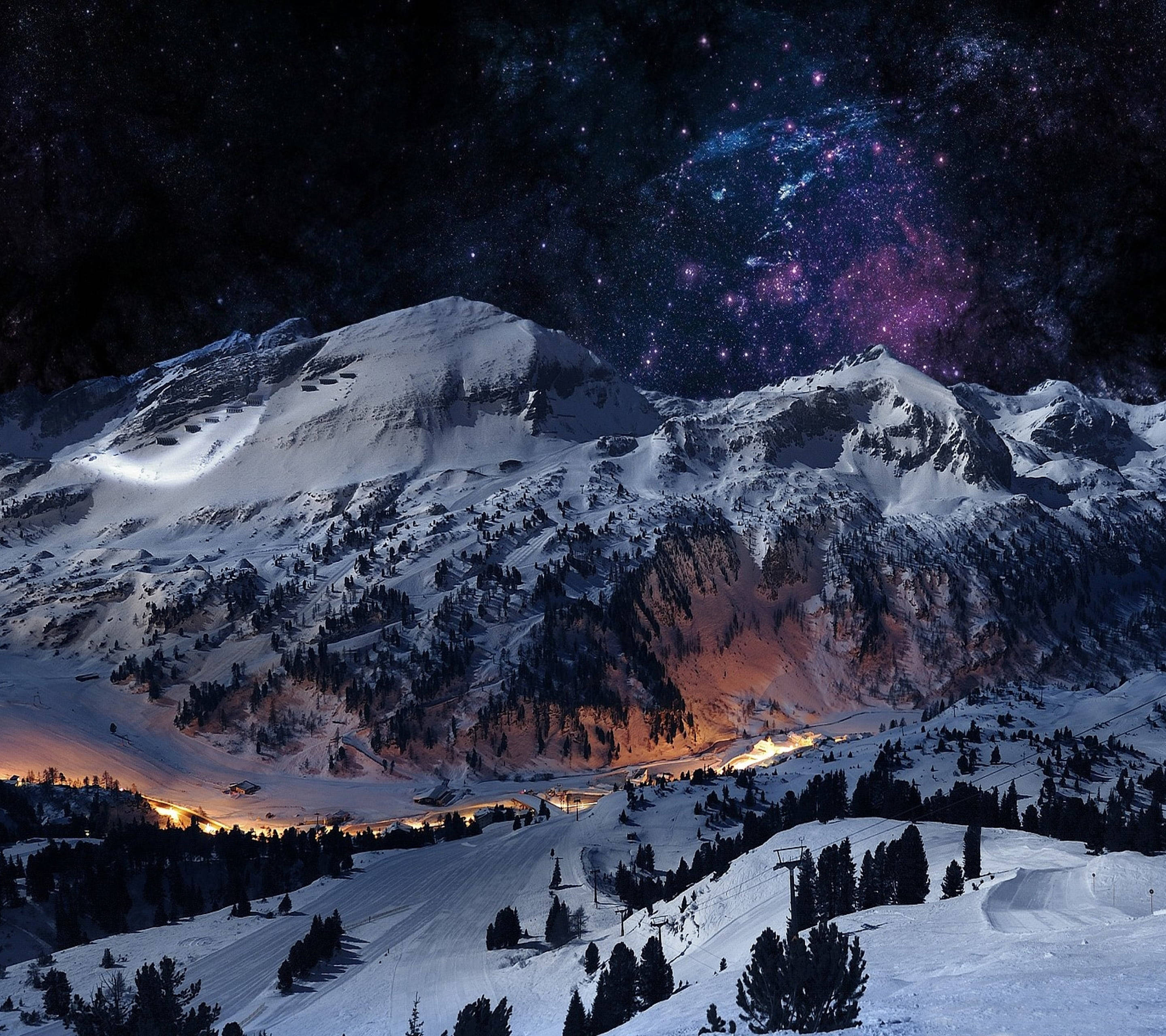 冬天 桌布 壁紙 — 白雪覆蓋的山峰，在充滿活力的紫色和藍色星空下，下方有發光的山谷燈光。