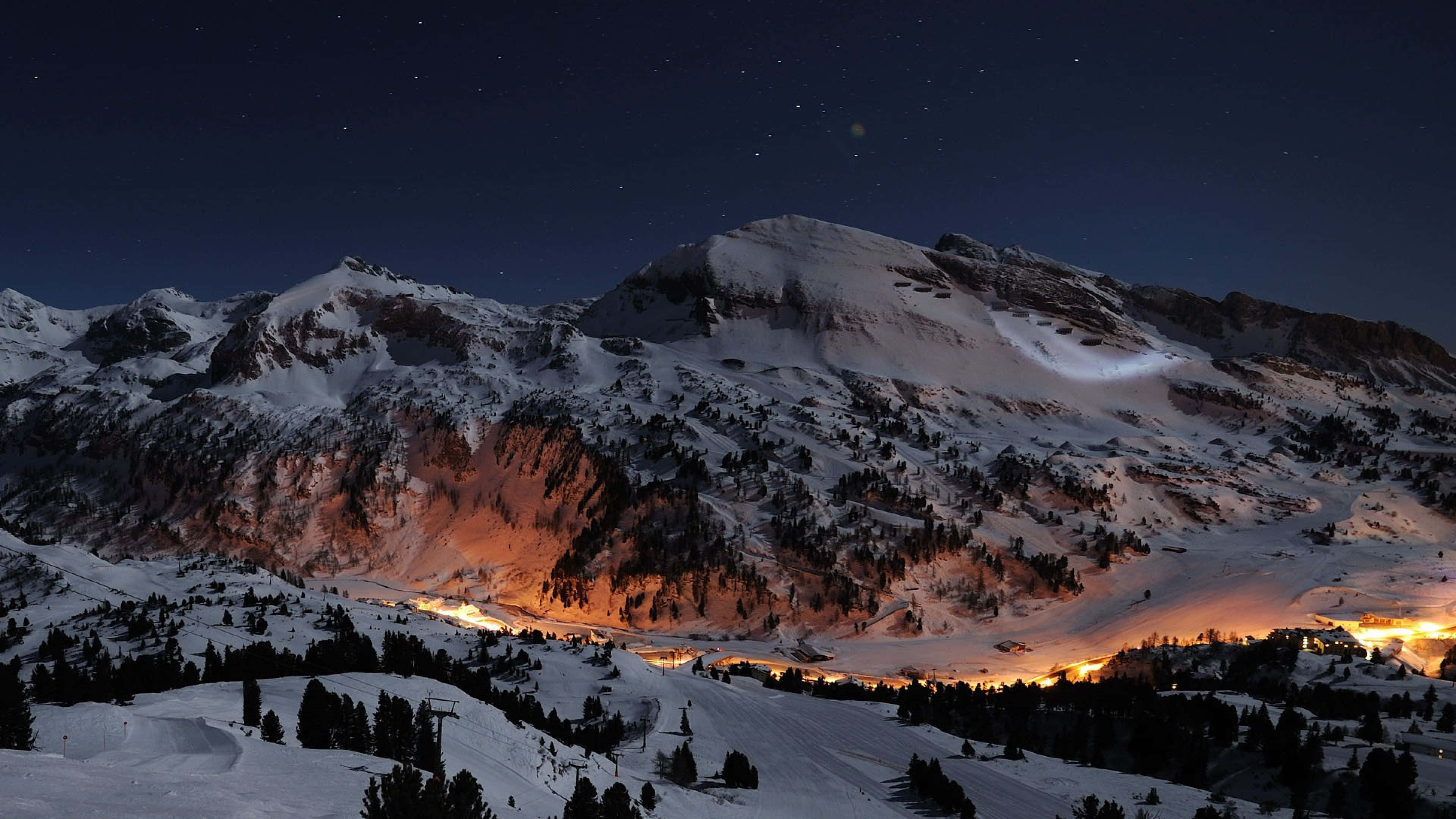 4K Mountain 桌布 壁紙 — 白雪覆蓋的山峰，在星空下，山谷中溫暖的燈光閃爍。