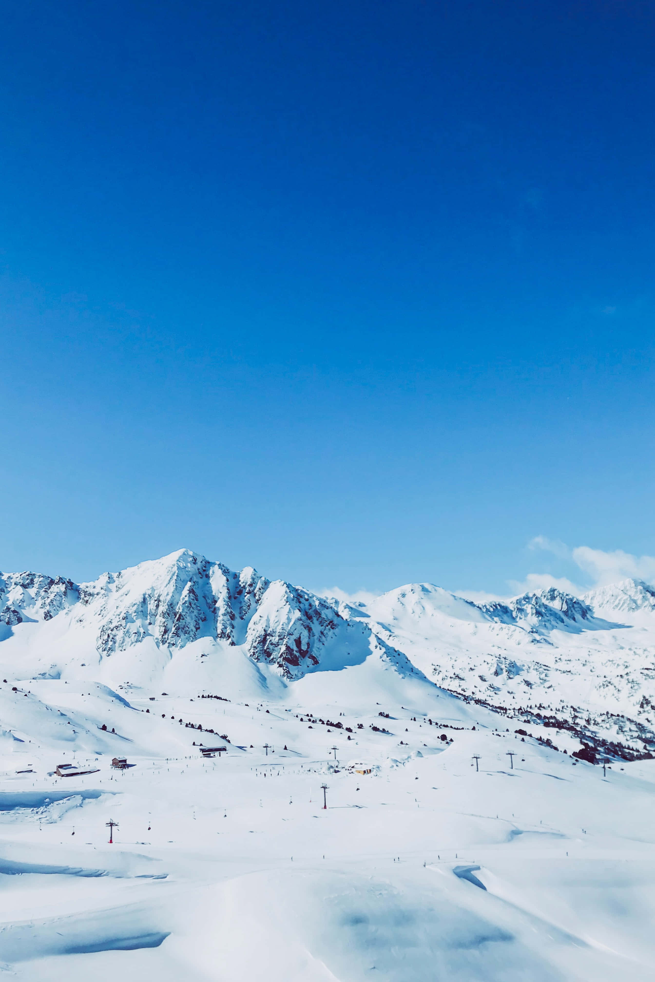 Ski Mountain 桌布 壁紙 — 白雪覆蓋的山峰，在清澈的藍天下，滑雪纜車和小型建築點綴在山坡上。
