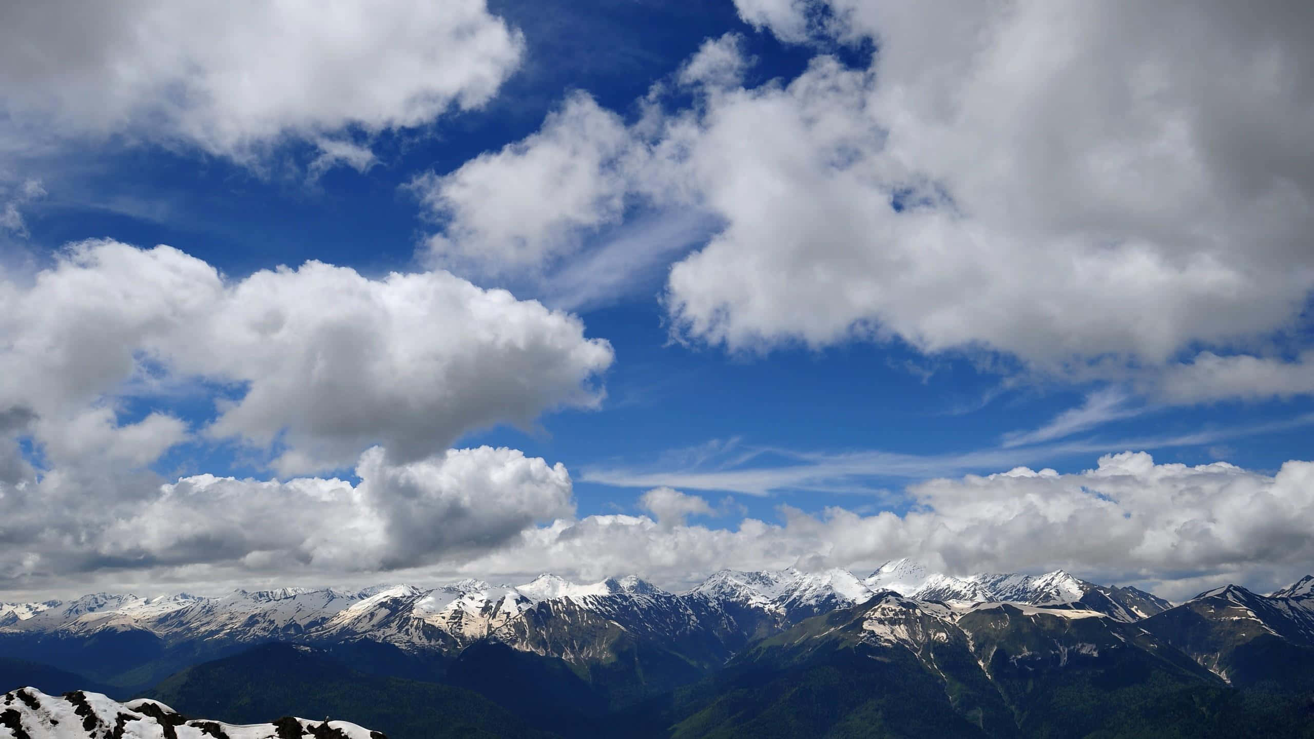 1440p 桌布 壁紙 — 白雪覆蓋的山峰刺穿充滿蓬鬆白雲的鮮豔藍天。