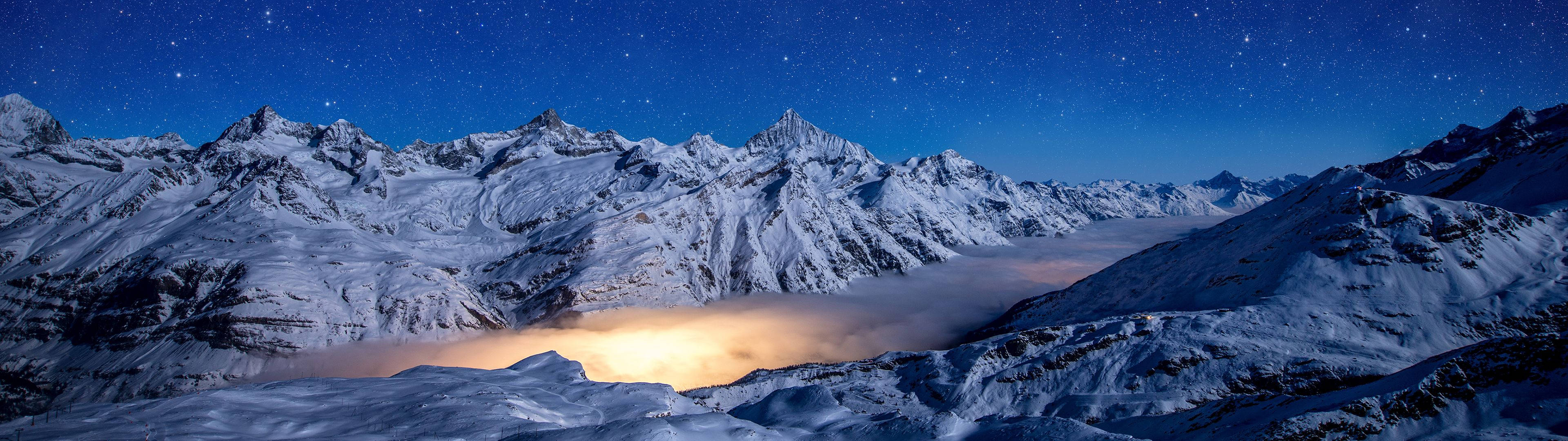 Dual 桌布 壁紙 — 白雪覆蓋的山峰刺穿星空，下方是發光的雲海山谷。