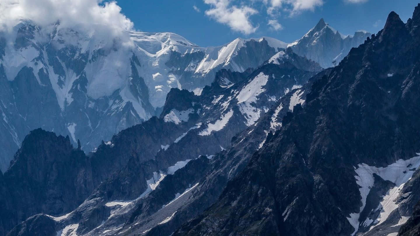 山景 桌布 壁紙 — 白雪覆蓋的山峰刺穿清澈的藍天，聳立在崎嶇的深色岩壁上，散落著斑駁的積雪。
