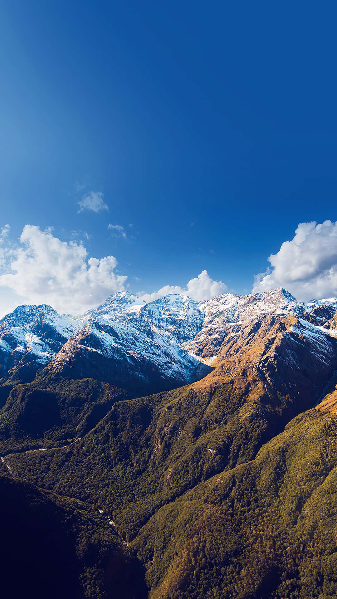 山景 桌布 壁紙 — 白雪覆蓋的山峰刺穿湛藍的天空，下方是沐浴在金色陽光中的翠綠山谷。