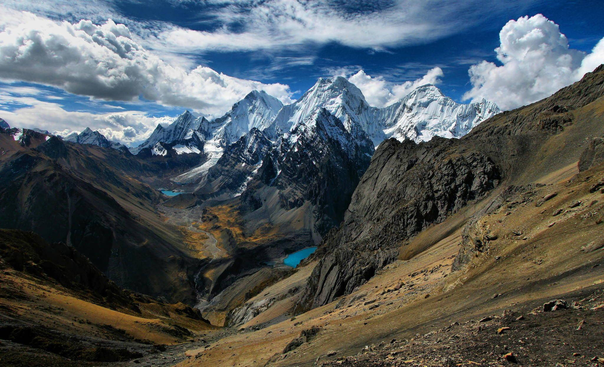 Peru 桌布 壁紙 — 白雪覆蓋的山峰刺穿湛藍的天空，蓬鬆的白雲飄浮在崎嶇的山谷之上，山谷中有一個碧綠色的湖泊。