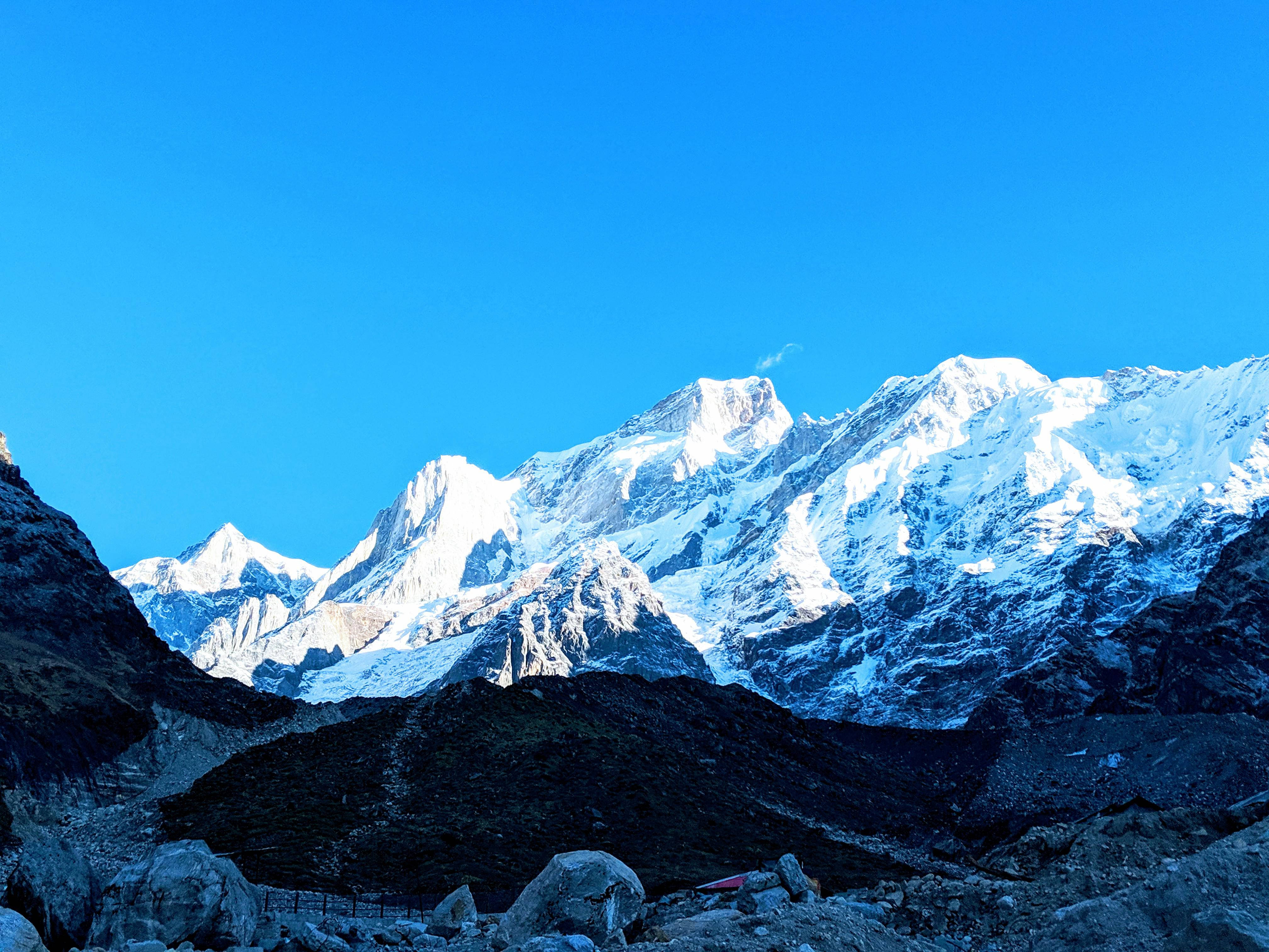 Kedarnath 桌布 壁紙 — 白雪覆蓋的山峰刺穿燦爛的藍天，下方是崎嶇的岩石地形。