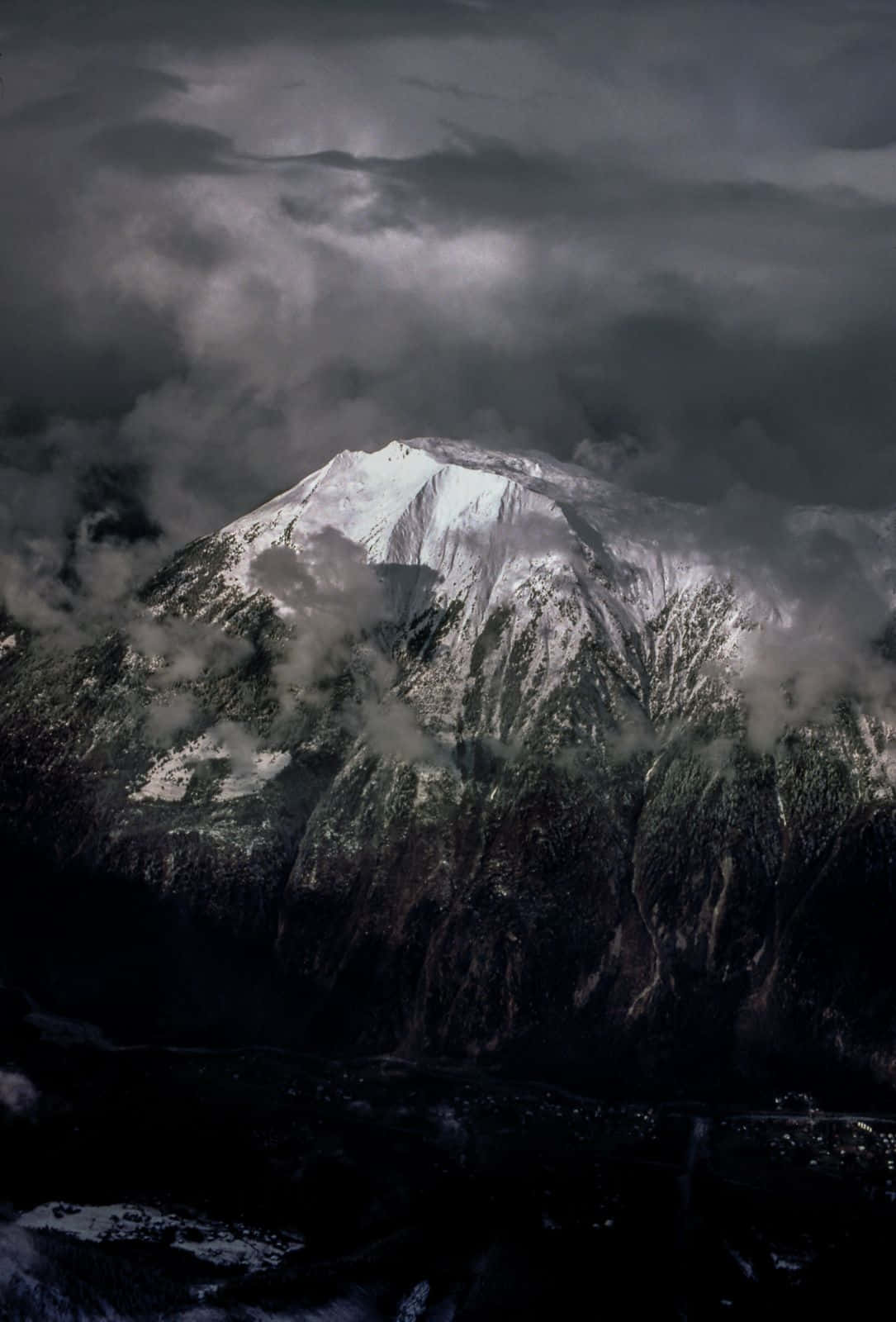 自然 桌布 壁紙 — 白雪覆蓋的山峰刺穿黑暗的暴風雲，霧氣在其崎嶇的山坡上盤旋。