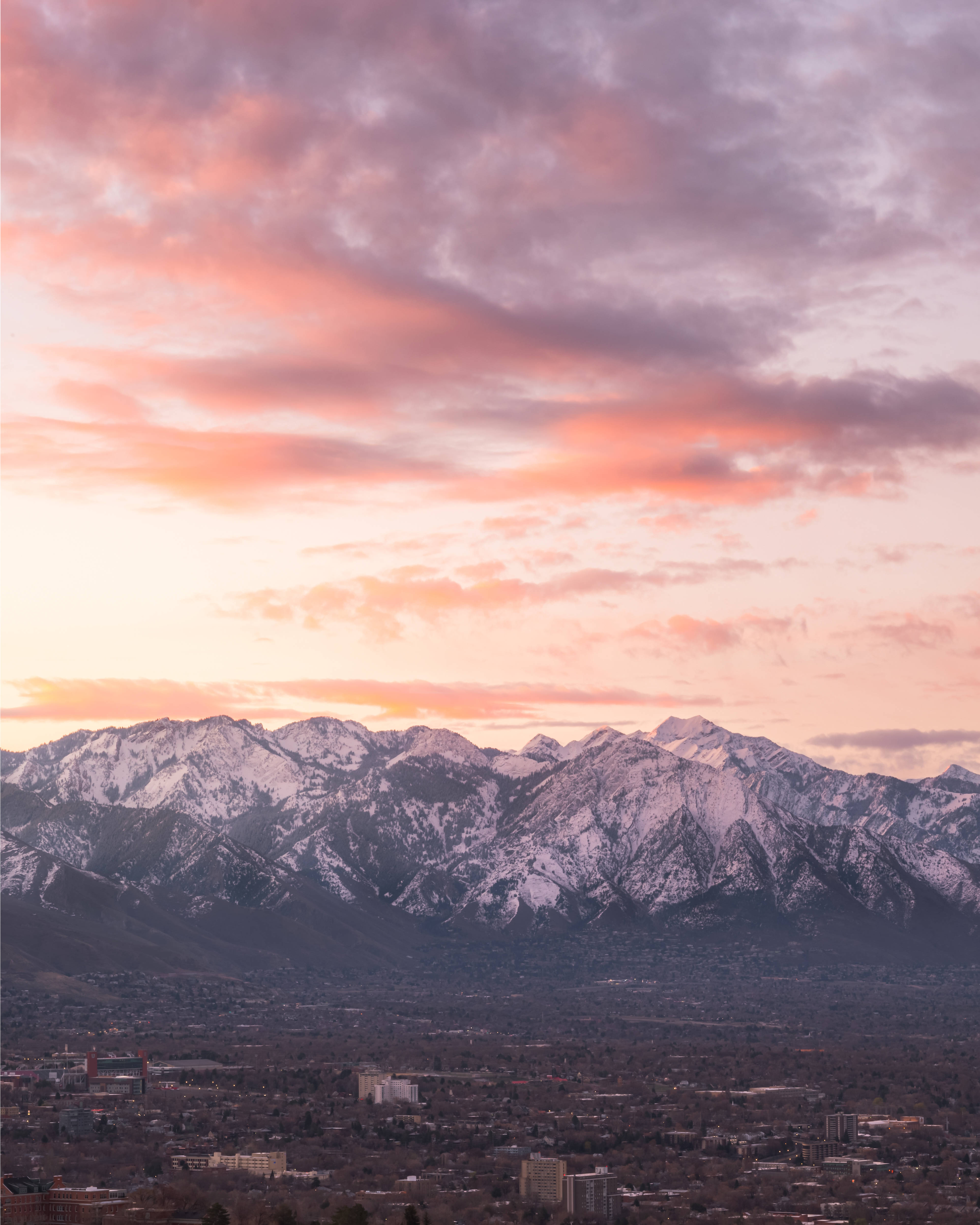 Salt Lake City 桌布 壁紙 — 白雪覆蓋的山峰在充滿活力的粉紅色和橙色日落天空下閃耀，下方是廣闊的城市景觀。