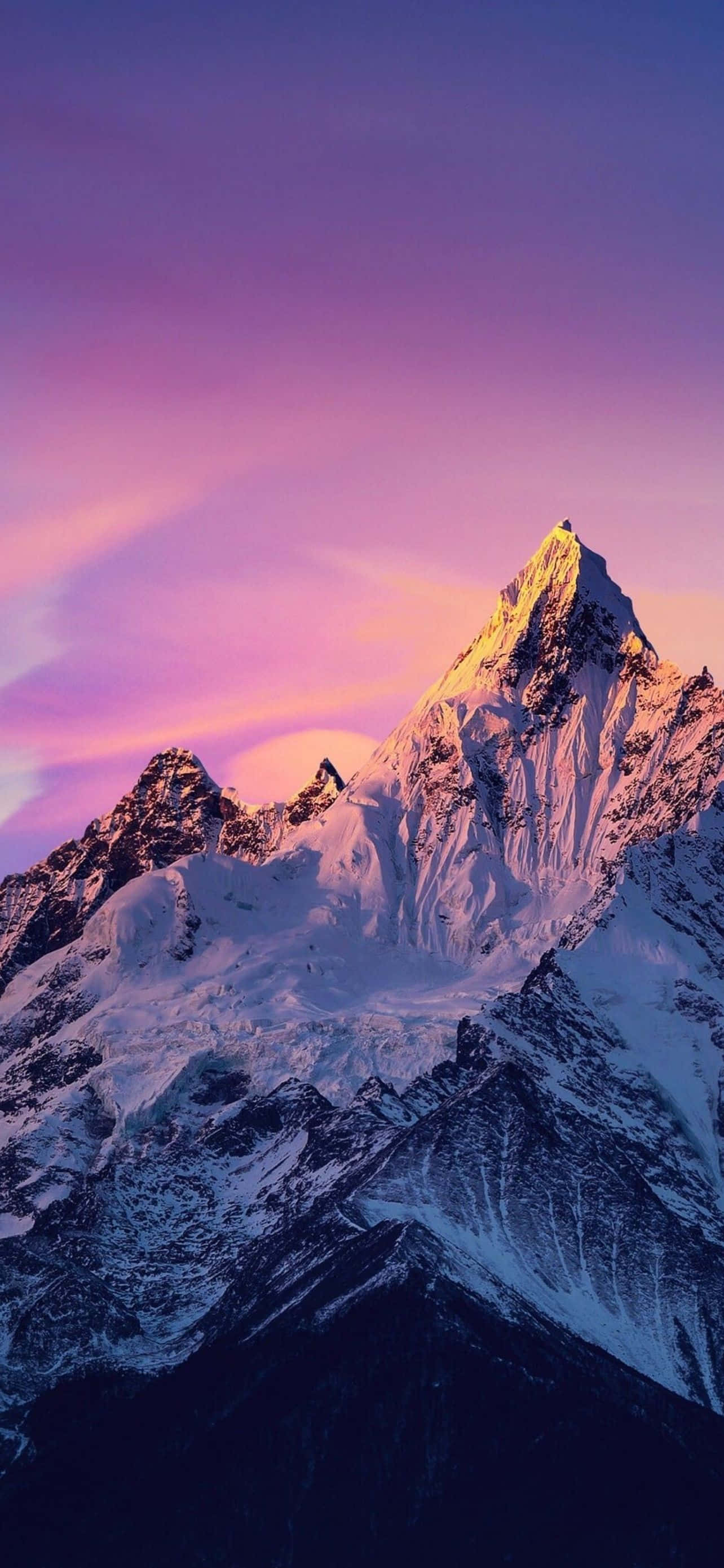 Mountain iPhone 桌布 壁紙 — 白雪覆蓋的山峰在充滿活力的紫色和粉紅色暮色天空下閃耀著金色光芒。