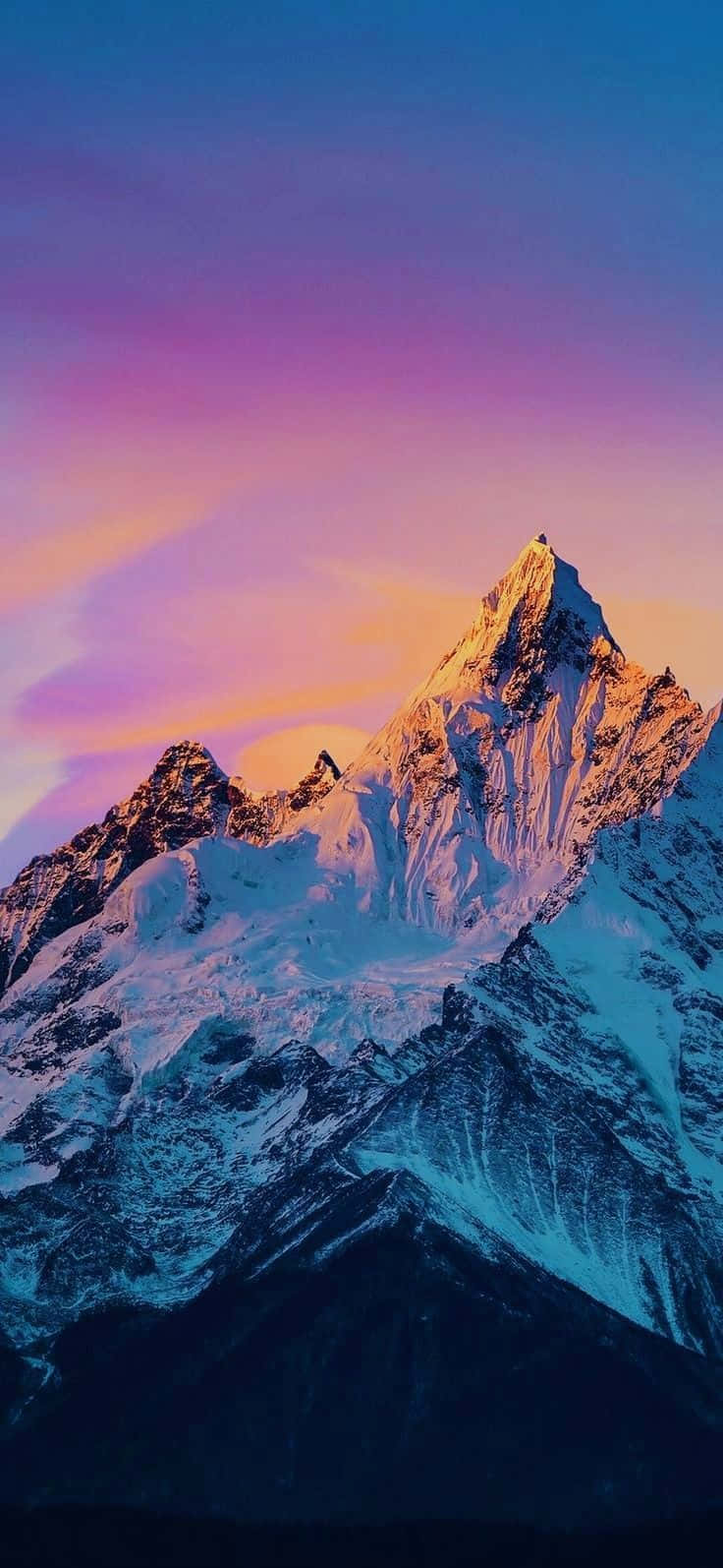 日落 桌布 壁紙 — 白雪覆蓋的山峰在充滿活力的紫色和粉紅色暮色天空中閃耀著金色的光芒。