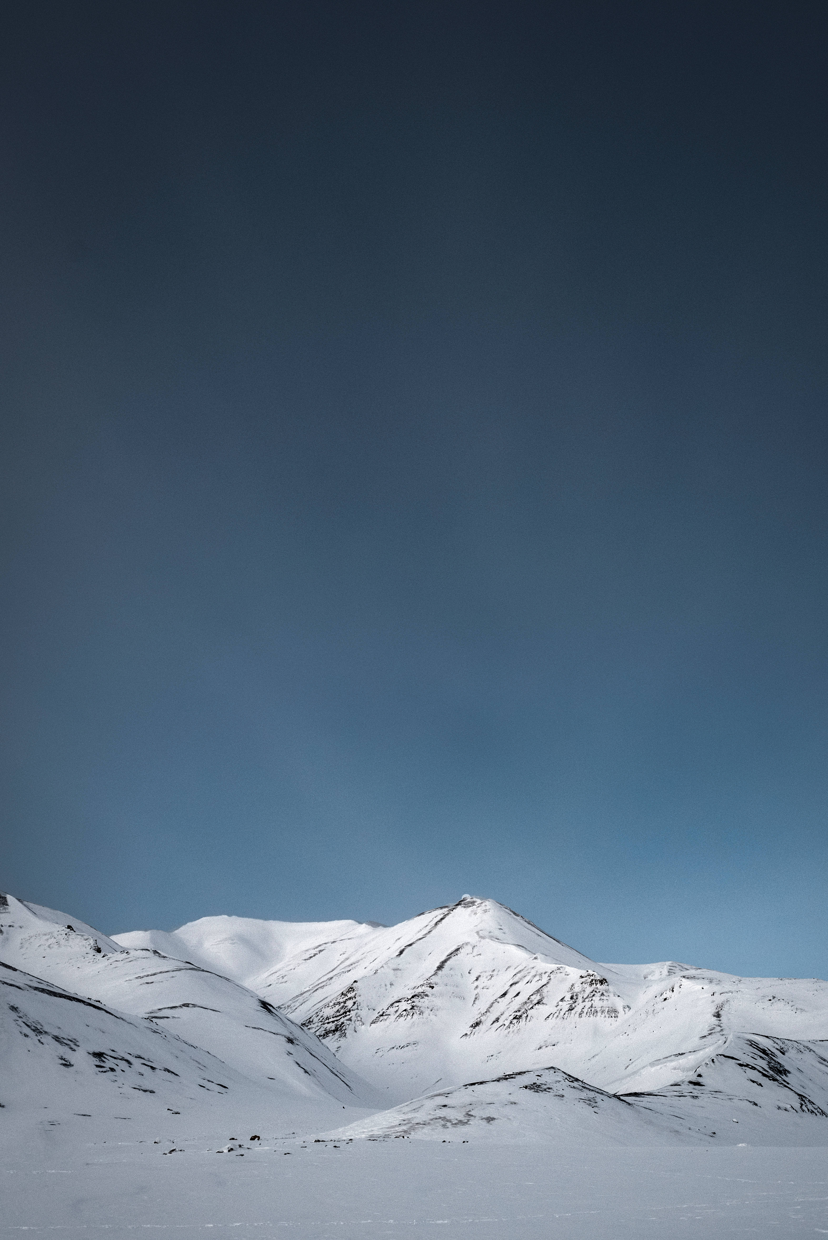 Svalbard 桌布 壁紙 — 白雪覆蓋的山峰在嚴冬景色中，於廣闊的漸層藍天下陡峭聳立。