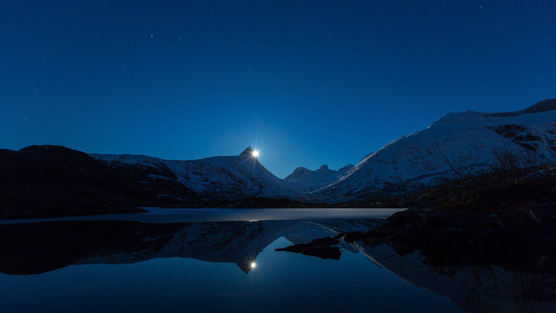 月光 桌布 壁紙 — 白雪覆蓋的山峰在夜晚明亮的星星下閃耀，其倒影完美地映照在下方平靜的湖面上。