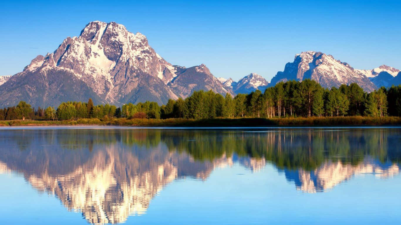 Mountain Landscape 桌布 壁紙 — 白雪覆蓋的山峰在平靜的湖泊後方雄偉地聳立，在清澈的藍天下倒映著它們的山巔。