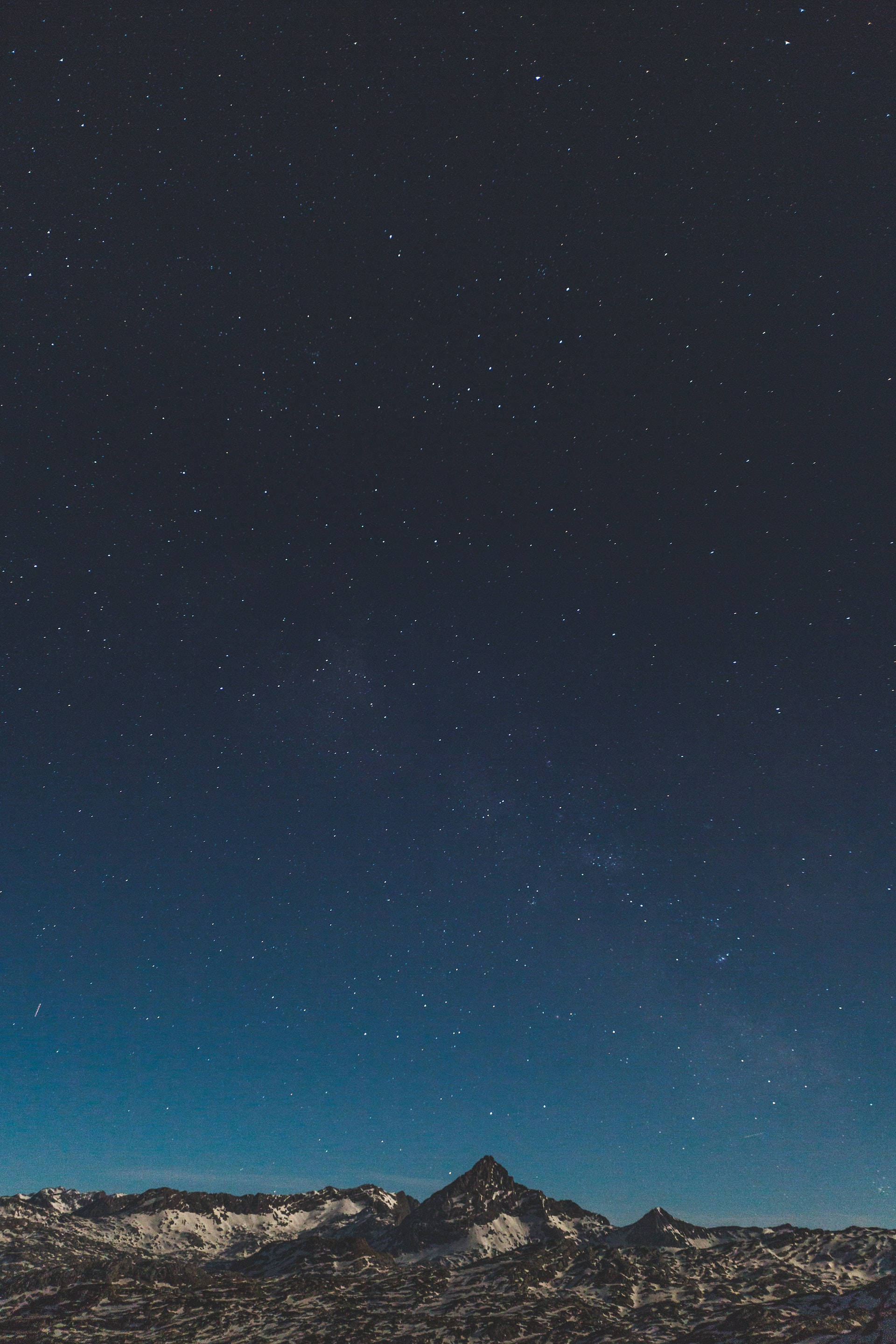 夜空 桌布 壁紙 — 白雪覆蓋的山峰在廣闊的星空下聳立，散發著宇宙藍和深靛藍的光芒。